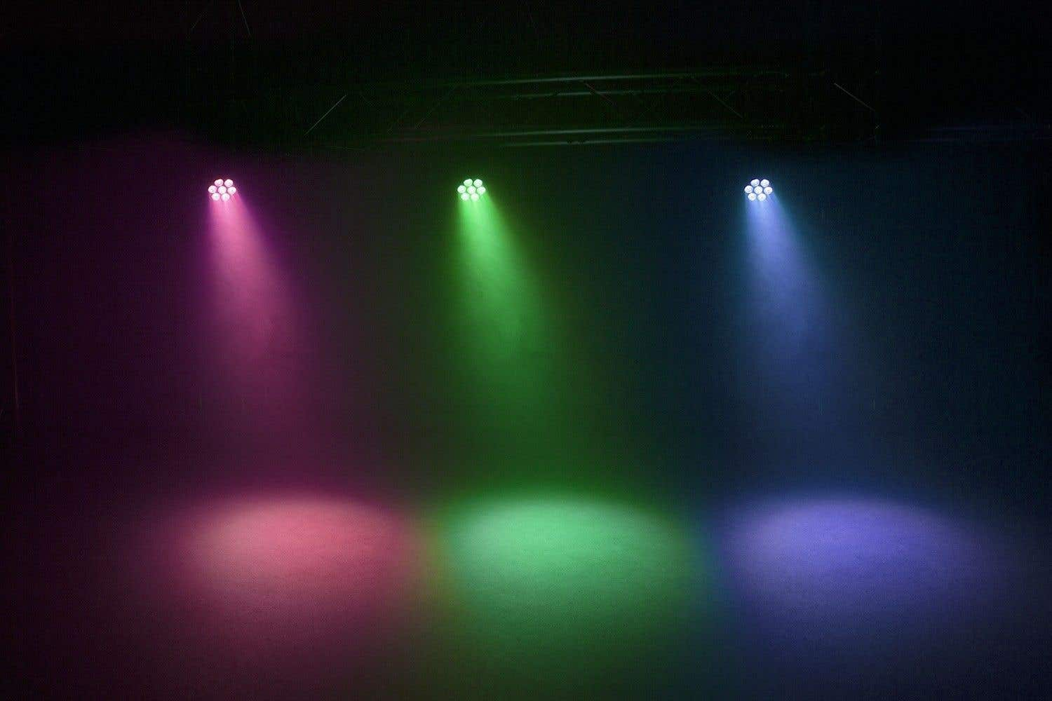 Tres focos brillan: rosa, verde y azul. Las luces iluminan el suelo, creando círculos de colores.