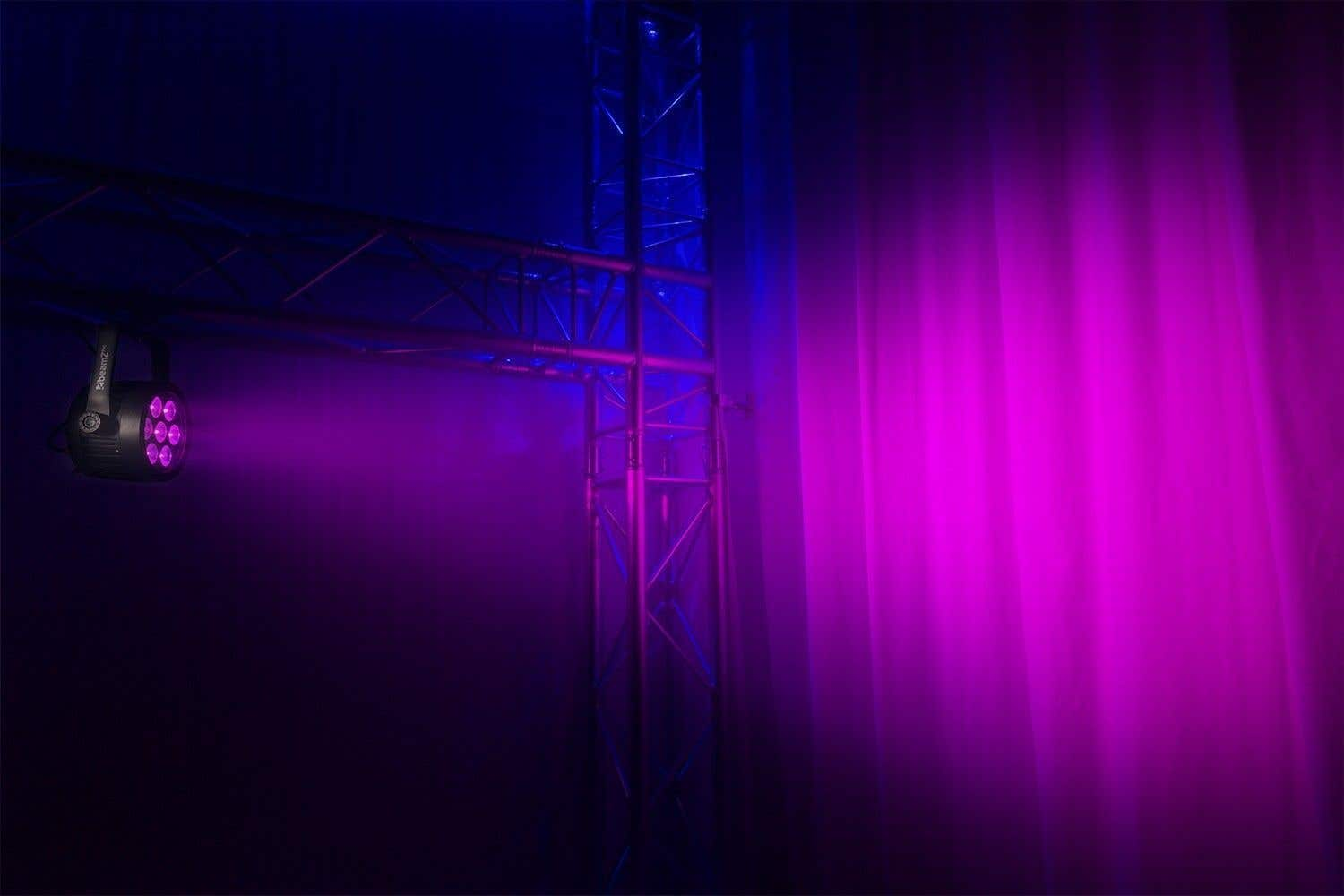Un escenario con iluminación púrpura y azul. Una luz de escenario está a la izquierda. Una estructura metálica está en el centro y a la derecha.