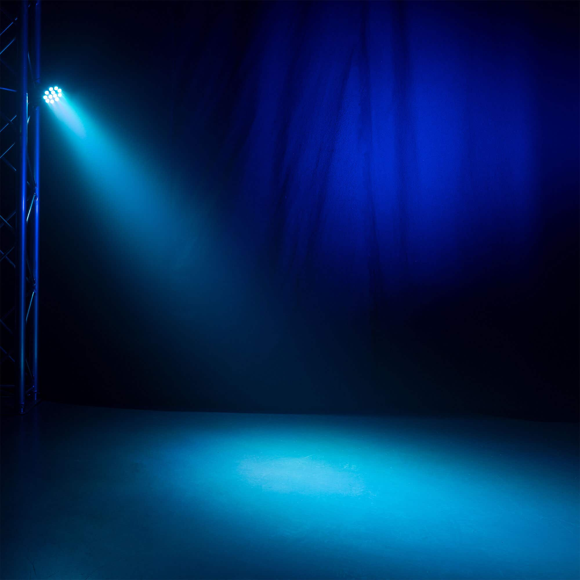 Un escenario iluminado por un foco azul brillante. Un marco de soporte de metal está a la izquierda. Fondo azul oscuro.