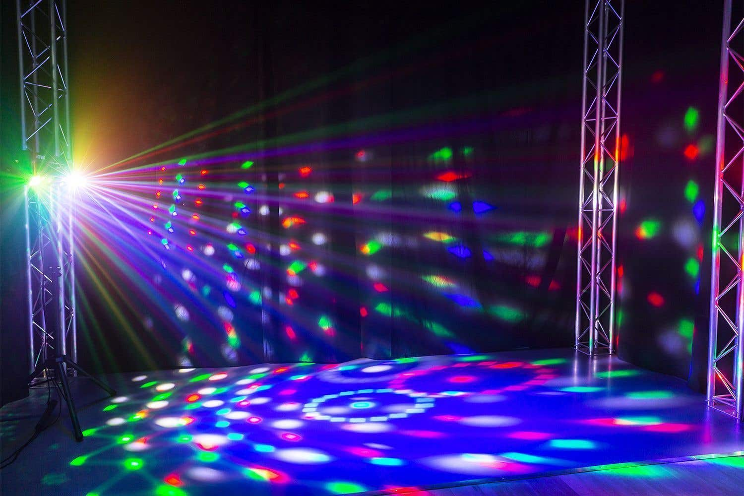 Un escenario con luces de colores. Los rayos de luz se proyectan sobre el escenario y el fondo. Andamios metálicos sostienen las luces.