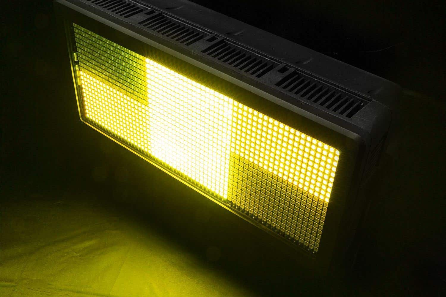 Un artefacto de luz LED rectangular con un brillo amarillo. El artefacto tiene un marco oscuro con un patrón de rejilla. El fondo es oscuro.