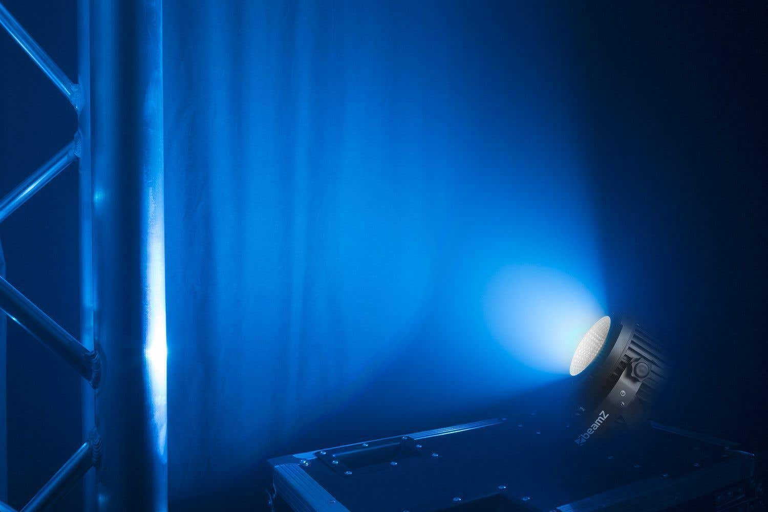 Una luz azul de escenario ilumina un fondo oscuro. Andamios metálicos a la izquierda. Una luz beamz en una caja en la parte inferior.