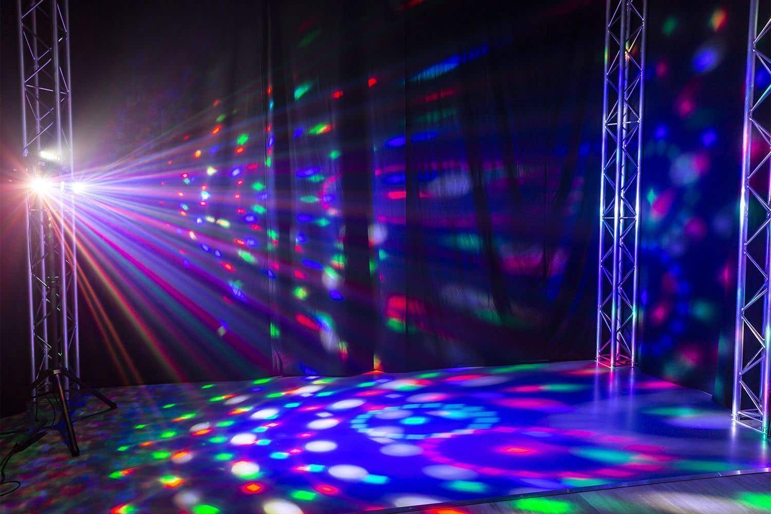 Un escenario iluminado por un foco con haces de luz coloridos. El suelo y el fondo también están iluminados con patrones coloridos.