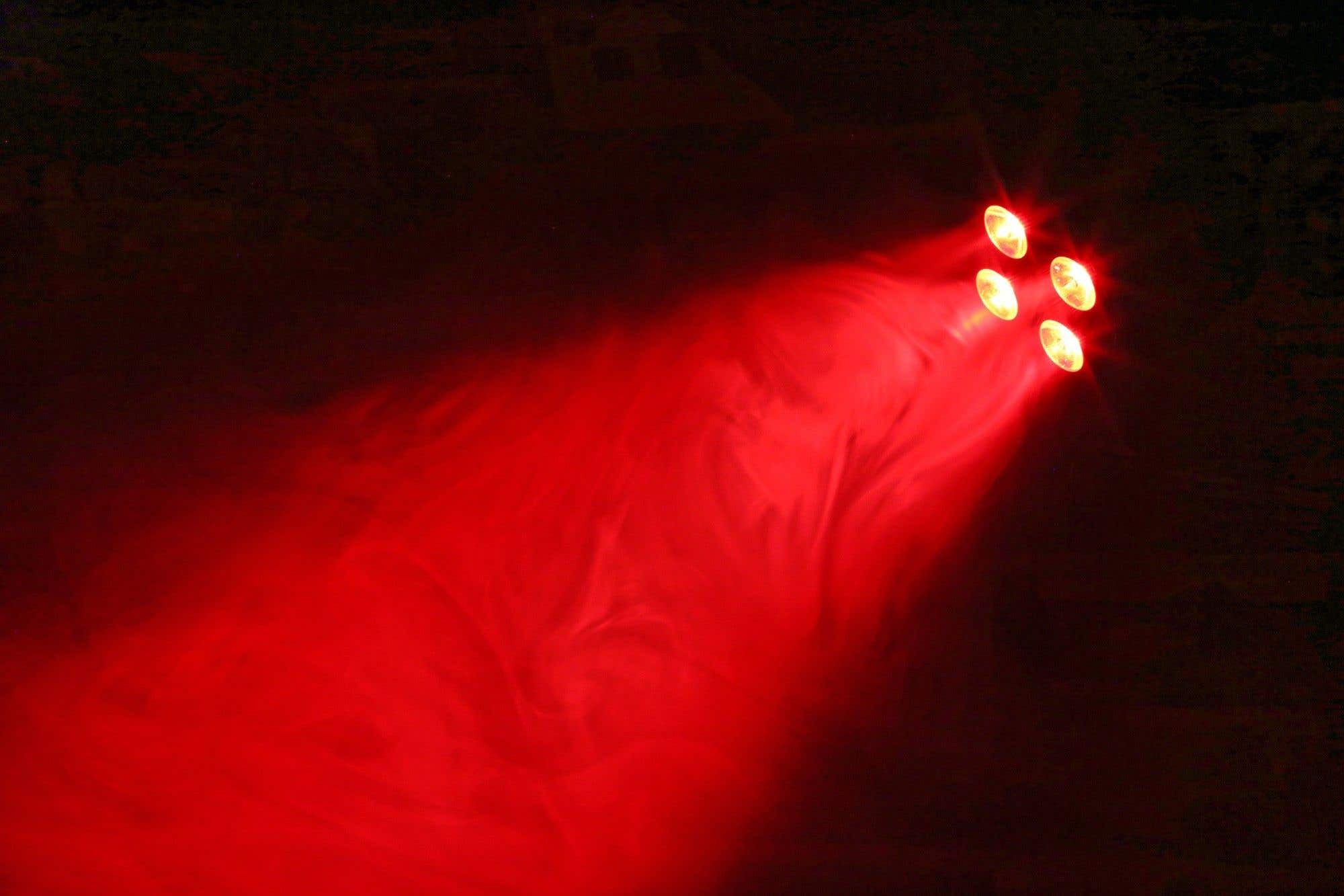 Cuatro luces brillantes brillan en rojo en un espacio oscuro, con un haz de luz roja que se extiende hacia abajo.