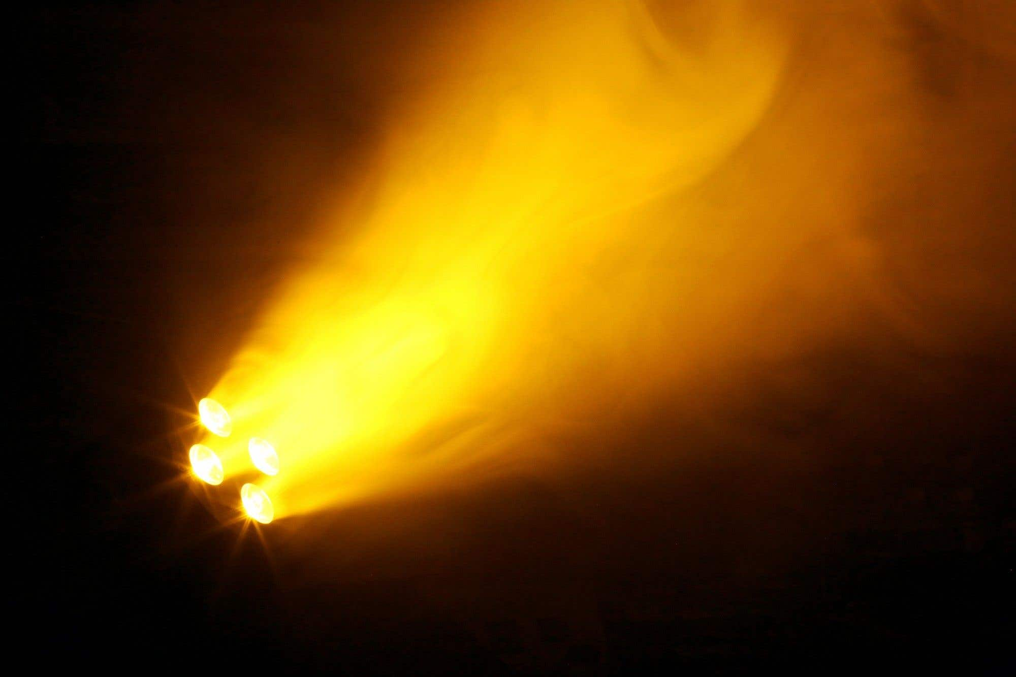 Cuatro luces amarillas brillantes brillan desde la izquierda inferior, creando un haz de luz contra un fondo oscuro, con algo de humo.