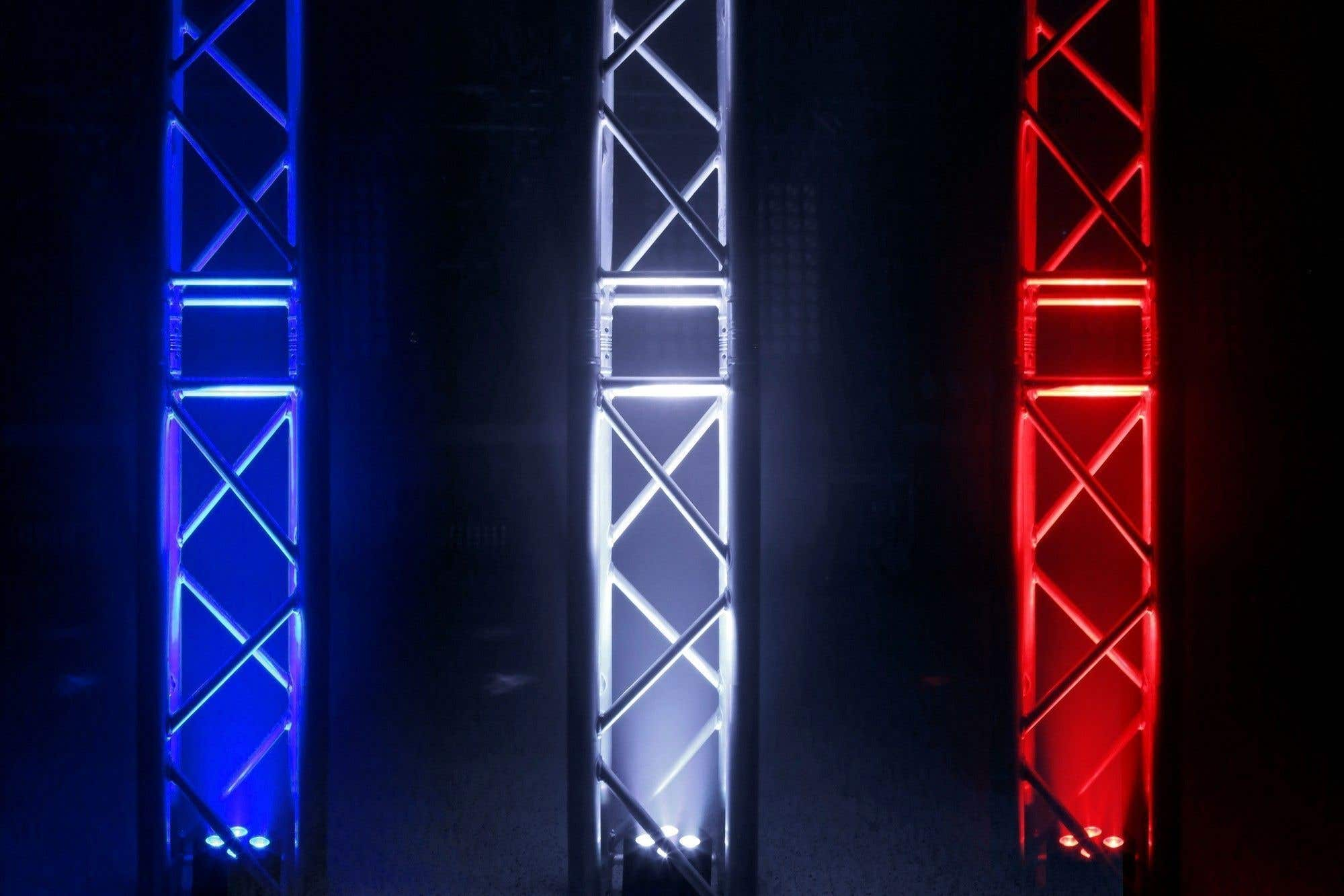 Tres estructuras metálicas iluminadas. Izquierda azul, centro blanco y derecha roja, sobre fondo oscuro.