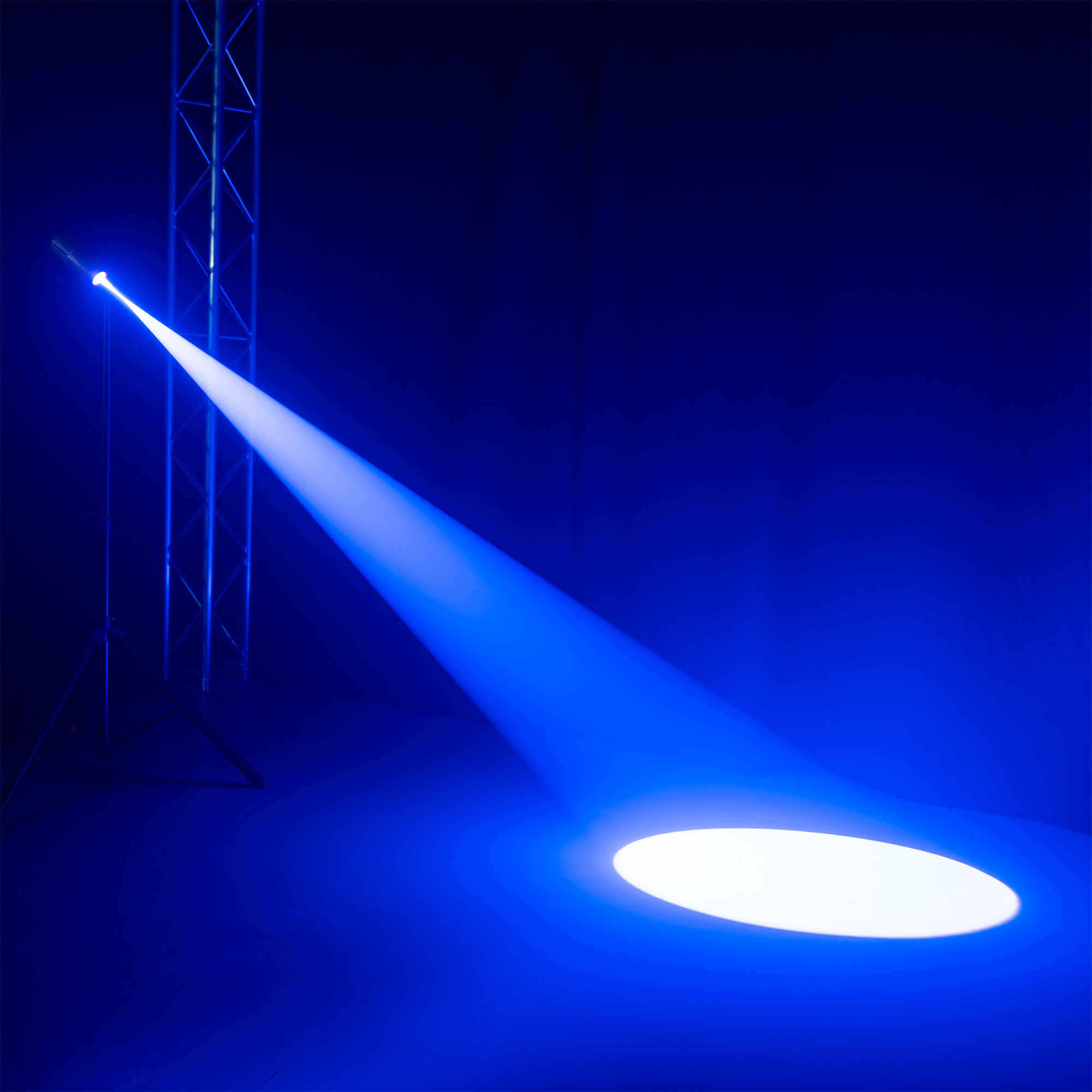 Un foco ilumina un rayo azul sobre un escenario oscuro. Una estructura metálica está a la izquierda. La luz crea un círculo blanco.