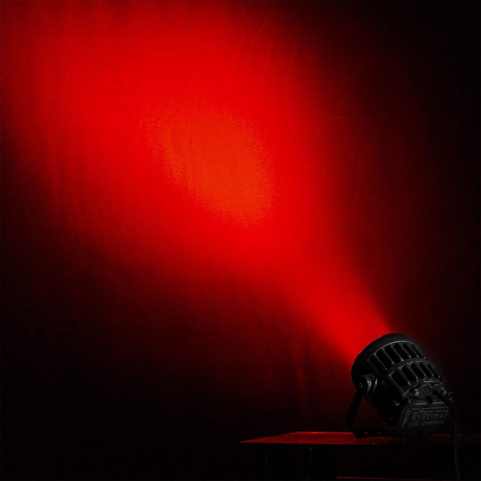 Un foco ilumina con luz roja una pared. El foco es negro, en la esquina inferior derecha.