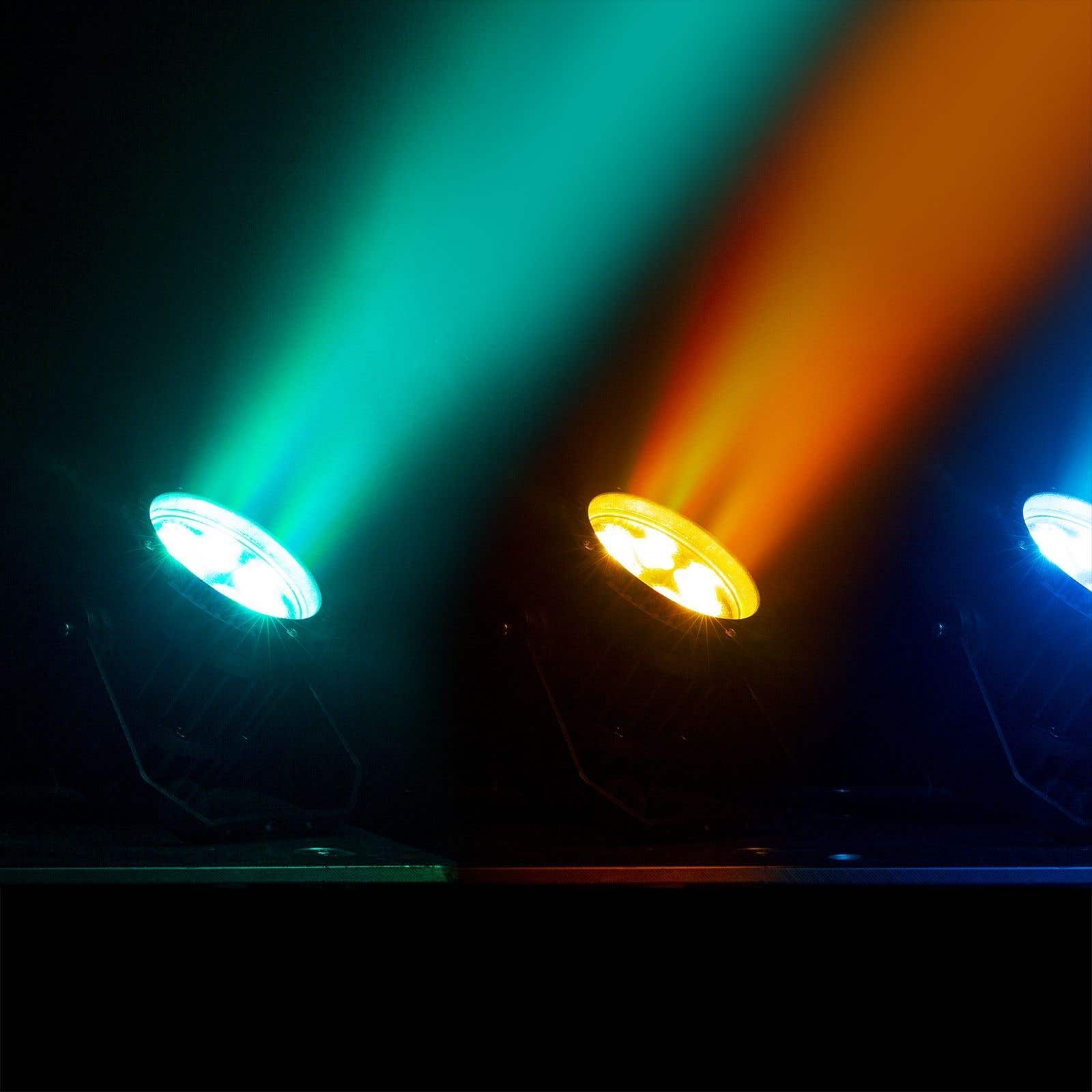 Tres focos iluminan la oscuridad con haces verdes, naranjas y azules. Las luces están sobre una superficie negra.