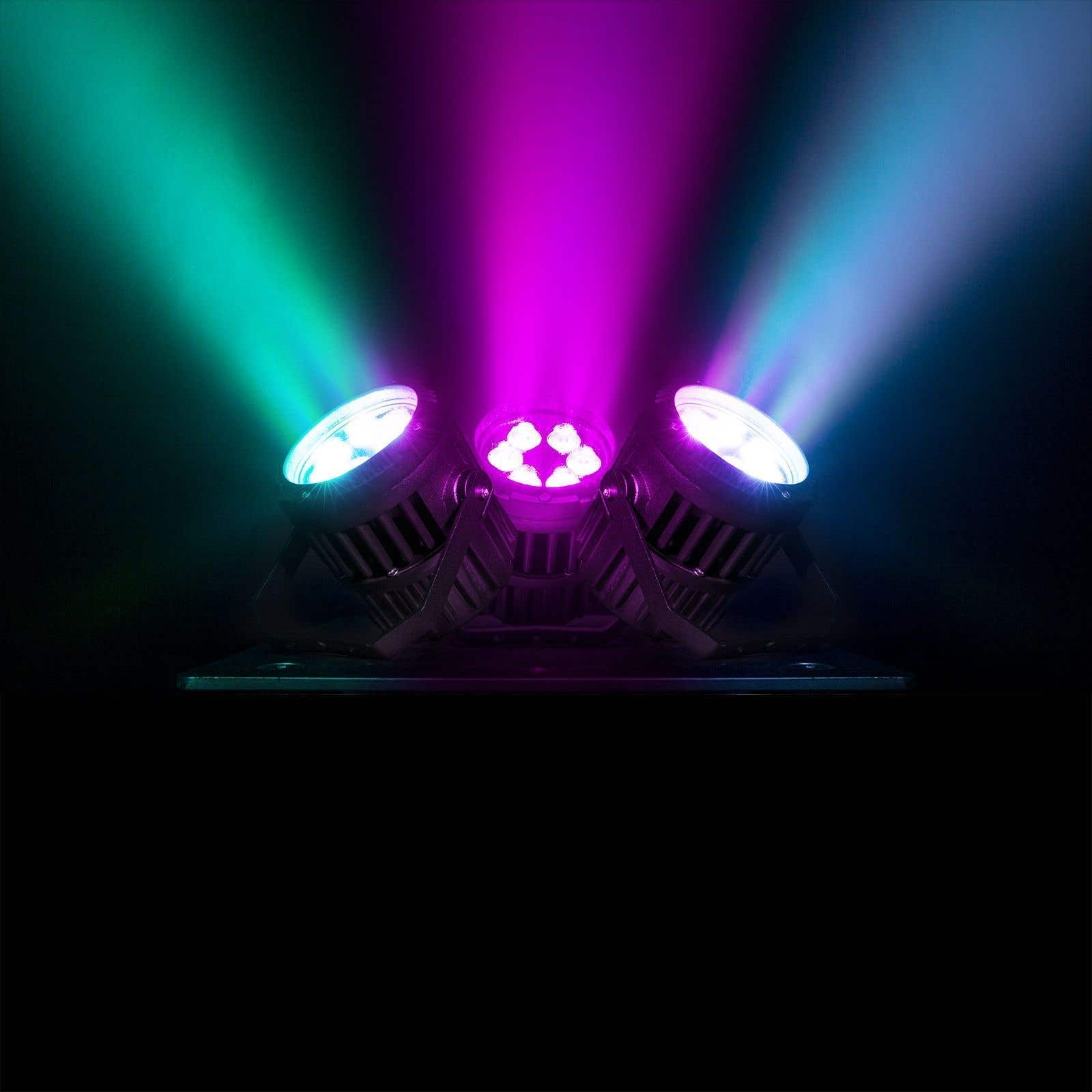 Tres focos proyectan rayos verdes, morados y azules sobre un fondo oscuro. Las luces están sobre una base de metal.
