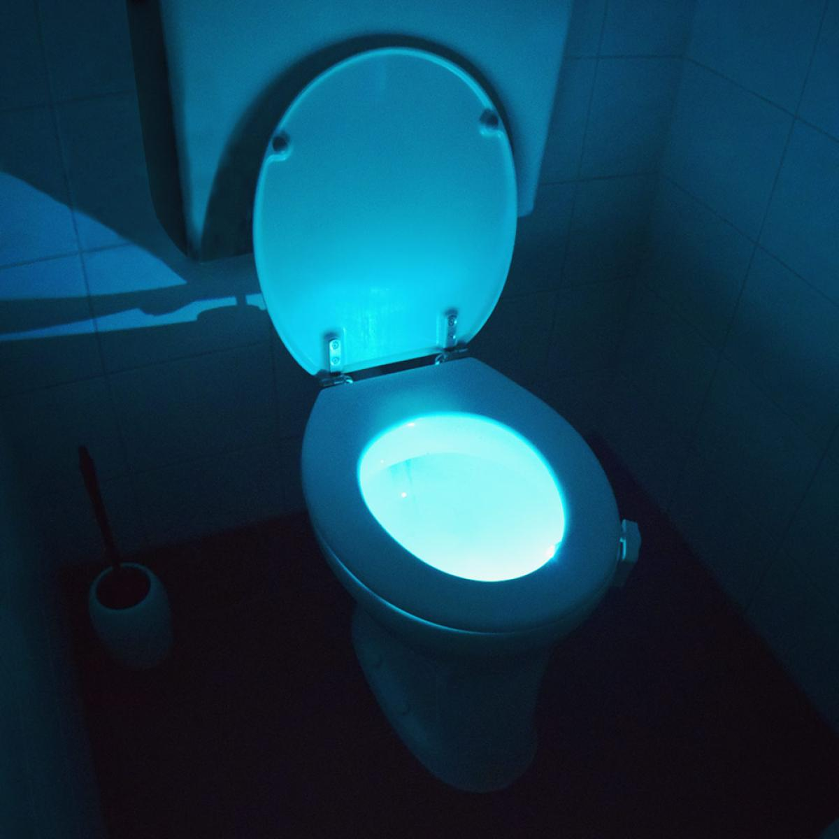 Een toilet met deksel omhoog en blauw licht. Er staat een borstel naast het toilet. De kamer is donker met witte tegels.
