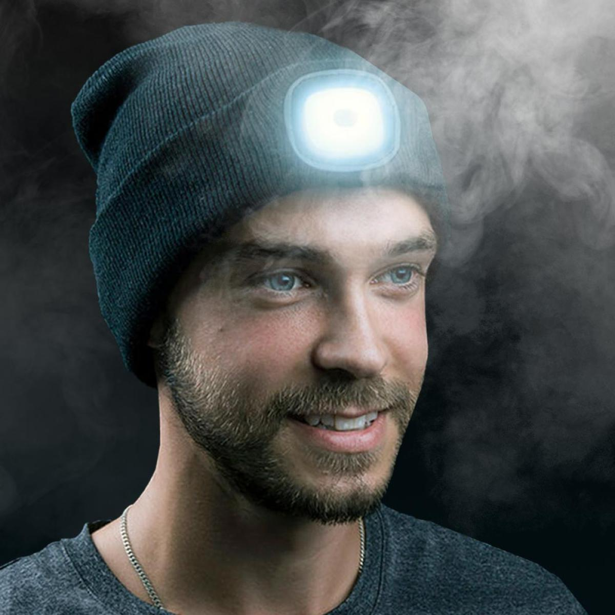 A man smiles, wearing a beanie with a lit LED light. He has blue eyes and a beard. Smoke drifts in the background.