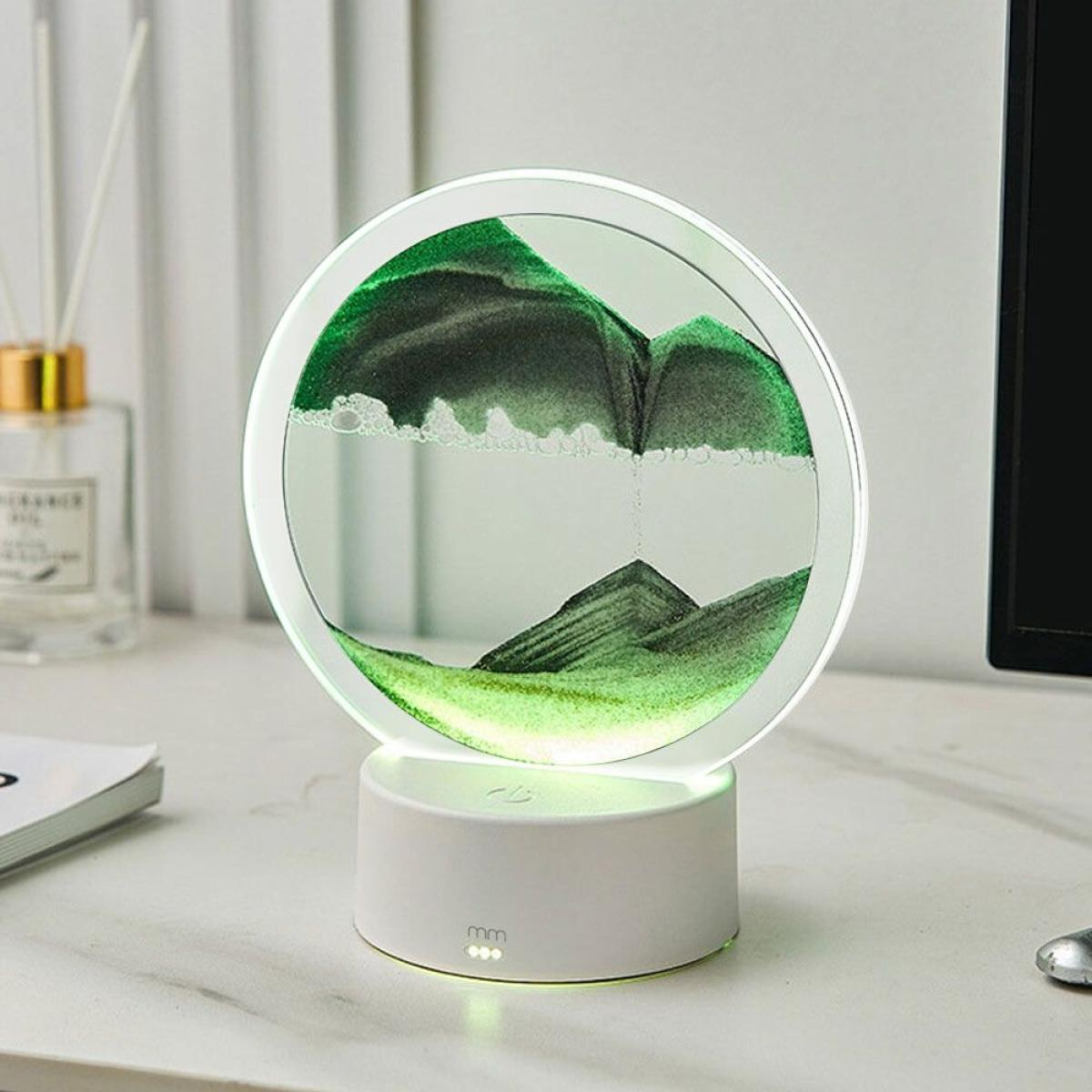 Een decoratieve zandkunstlamp toont een groene bergscène in een cirkelvormig glas. Hij staat op een witte basis.