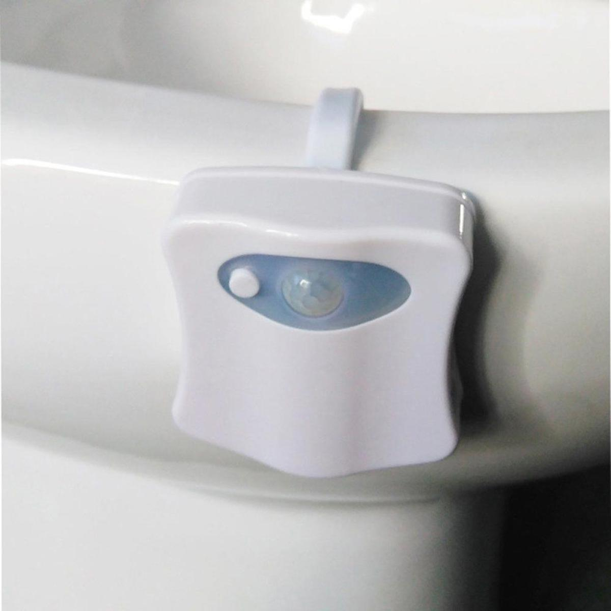 Een witte toiletpot met een wit apparaat bevestigd. Het apparaat heeft een blauwe sensor en is waarschijnlijk een nachtlampje.