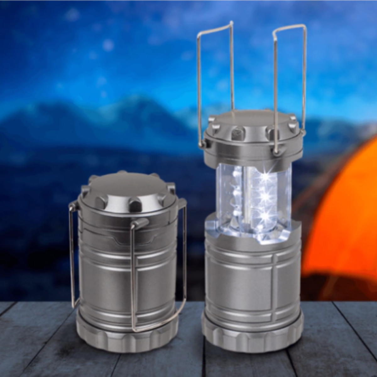 Two silver camping lanterns on a wooden surface. One is closed, the other is open and illuminated with white lights. Tent in background.