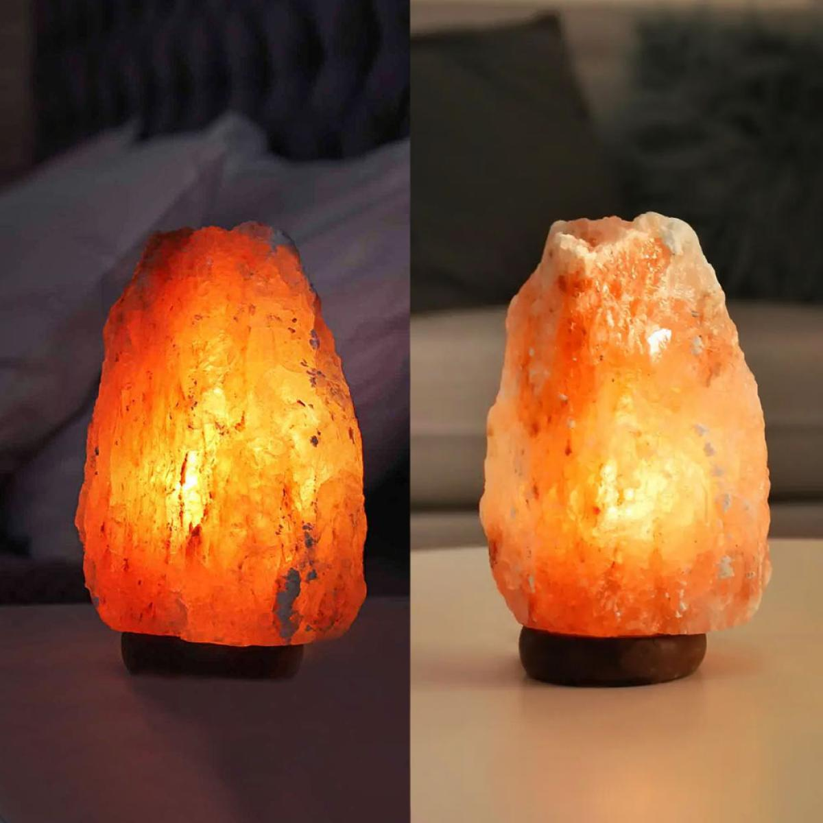 Twee zoutlampen staan op een tafel. De lampen zijn oranje en verlicht, rustend op houten voetstukken. Achtergrond is een donkere kamer.