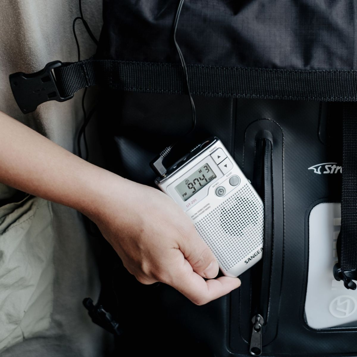 Ręka trzyma srebrne radio z gniazdem słuchawkowym. Radio jest w czarnej kieszeni. Wyświetlacz pokazuje 97,4.