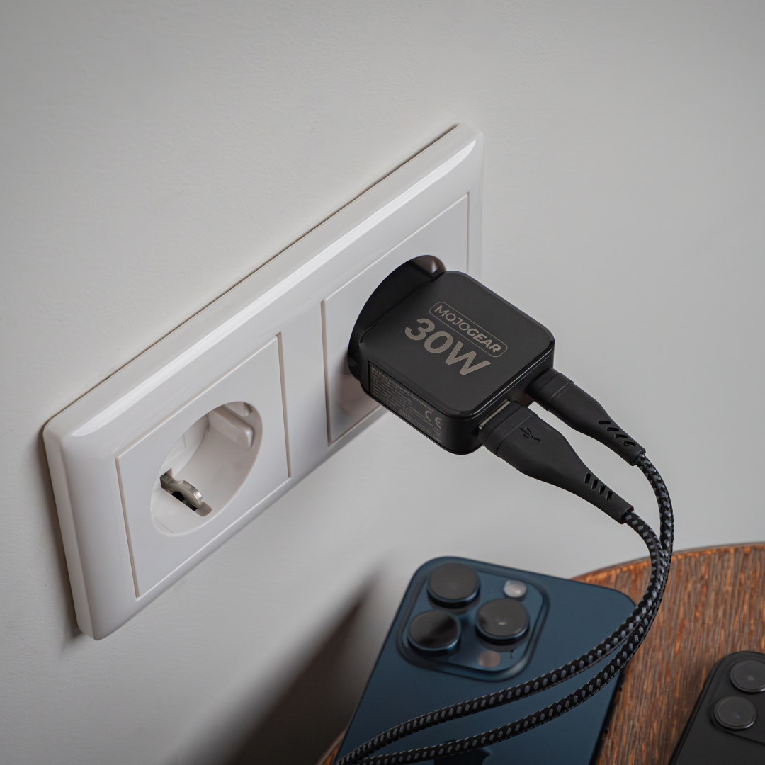 Ein schwarzes MojoGear 30W Ladegerät ist in eine Steckdose gesteckt. Zwei Ladekabel sind mit dem Ladegerät verbunden. Ein Telefon befindet sich darunter.