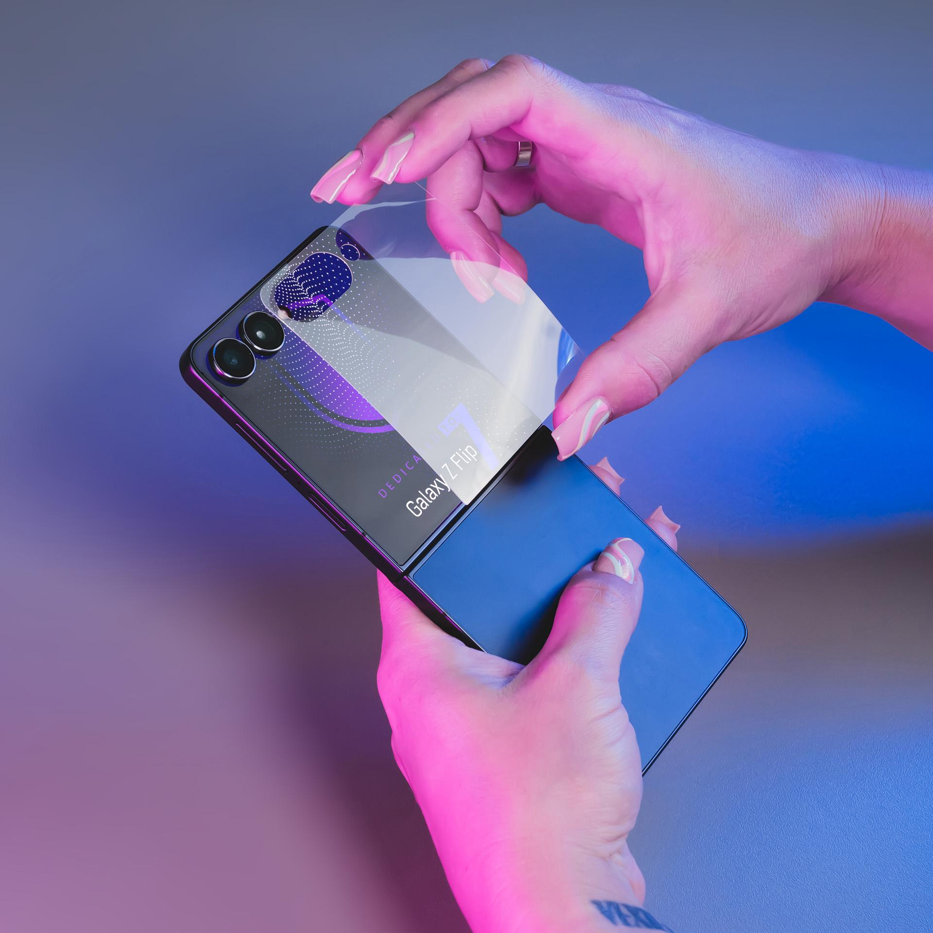 Mani applicano una protezione schermo su un telefono Samsung Galaxy Z Flip. L'illuminazione rosa e blu crea uno sfondo vivace.