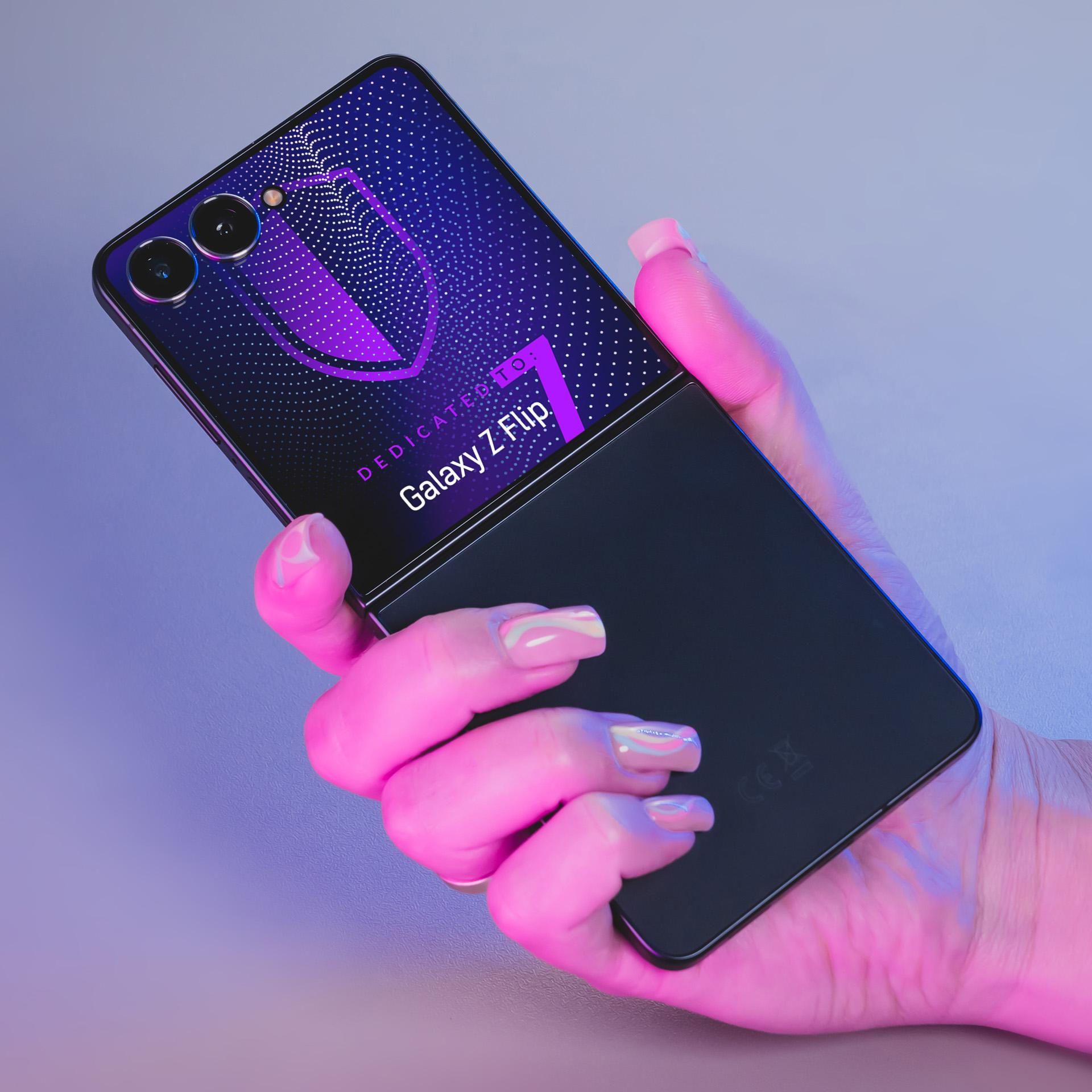 Una mano tiene in mano un telefono Galaxy Z Flip parzialmente aperto. Lo schermo mostra un design. Illuminazione rosa e blu.