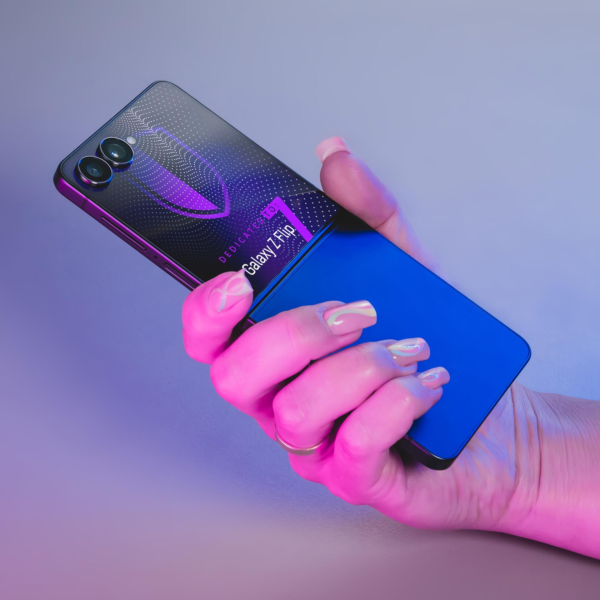 Una mano tiene un telefono blu parzialmente piegato. Il telefono è nero con dettagli viola e ha due fotocamere.