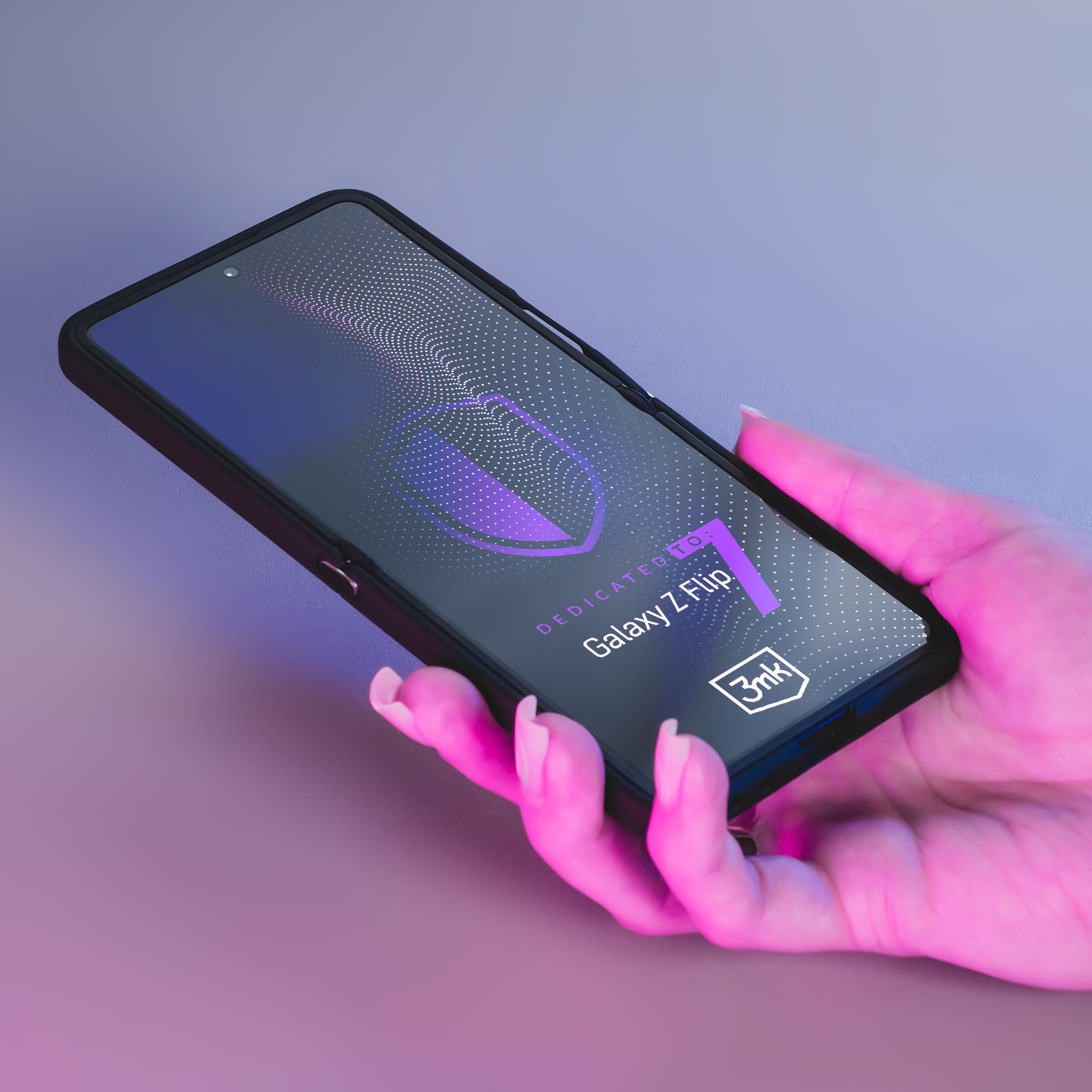 Dłoń trzyma telefon. Ekran wyświetla 'Galaxy Z Flip'. Tło jest fioletowe i różowe.