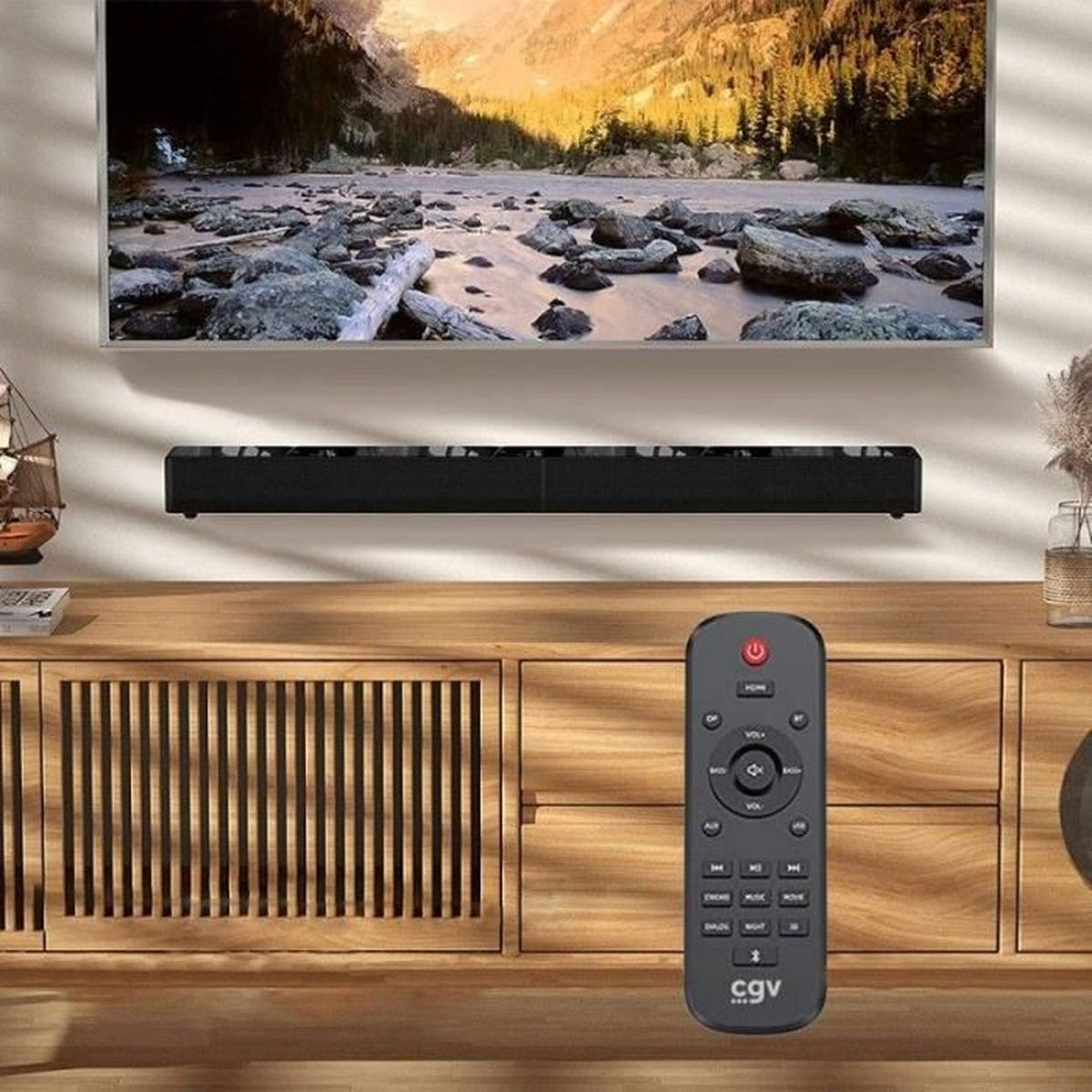 Ein Fernseher zeigt eine Berglandschaft. Darunter befindet sich eine Soundbar und davor eine Fernbedienung. Darunter ein Holzschrank.
