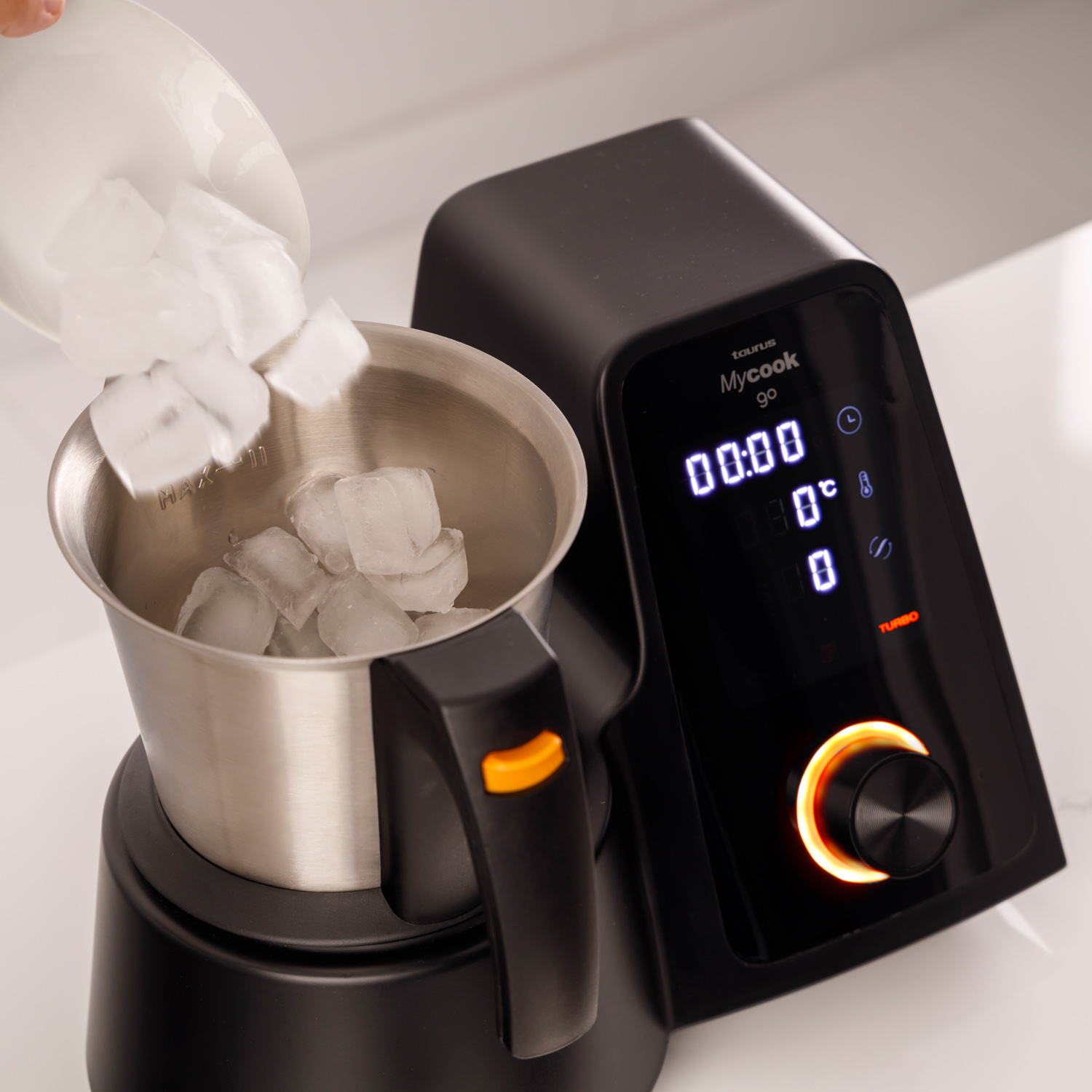 Cubitos de hielo se vierten en un cuenco de metal dentro de una máquina Mycook Go negra. La pantalla muestra la hora y la temperatura.