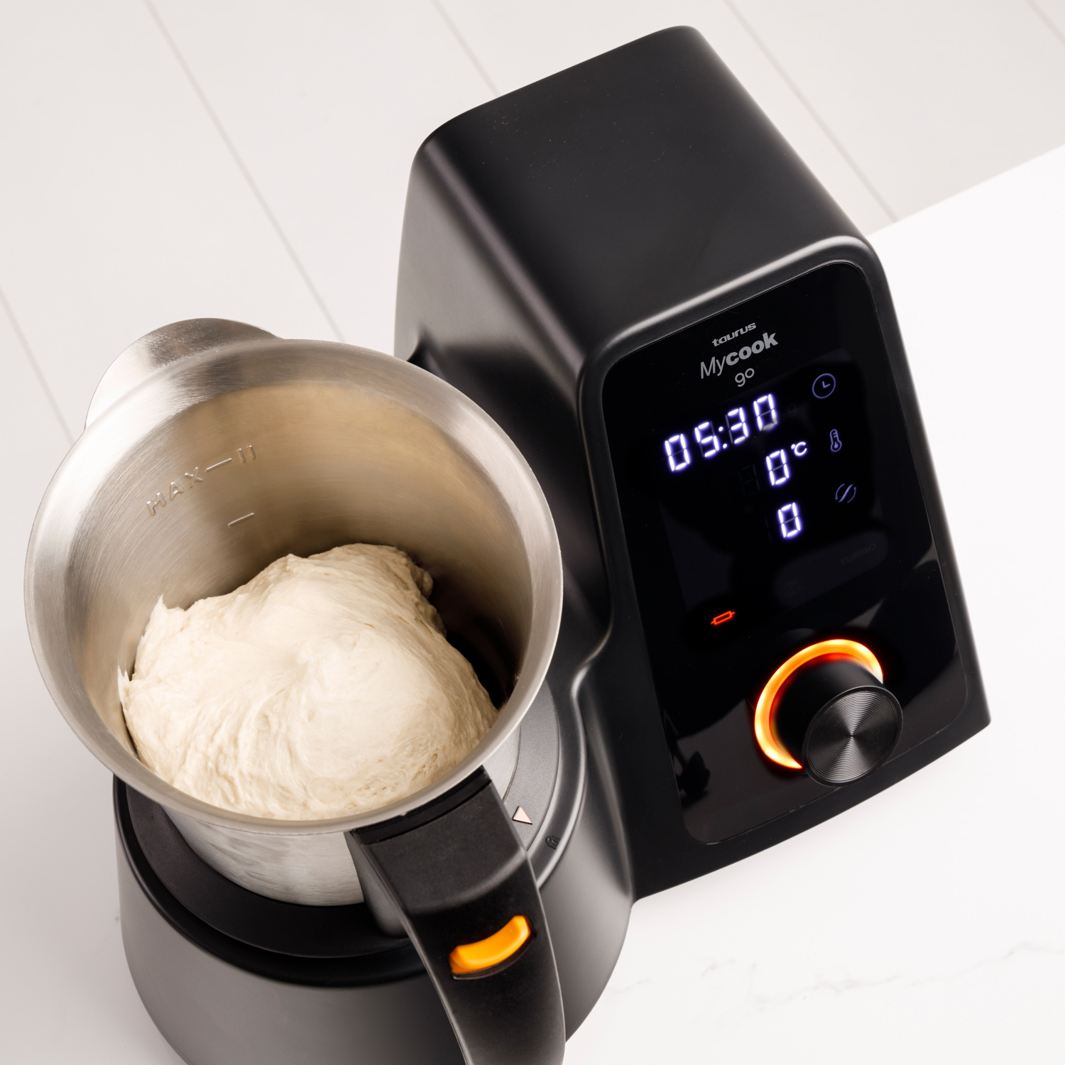 Un procesador de alimentos con masa dentro. La máquina es negra con una pantalla digital. El fondo es una superficie blanca.