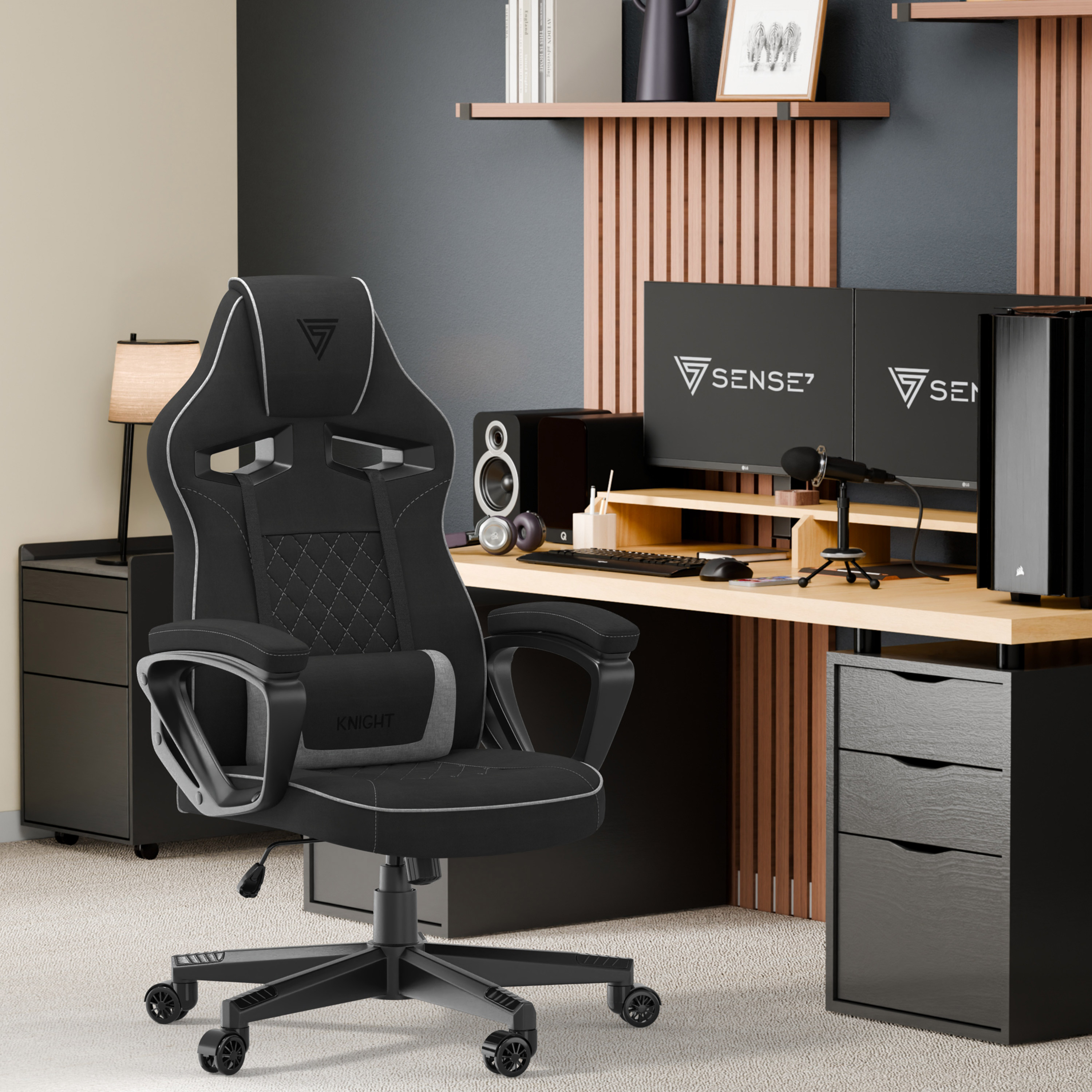 Configuration de jeu avec chaise noire, deux moniteurs, haut-parleurs et micro sur bureau en bois avec tiroirs noirs.