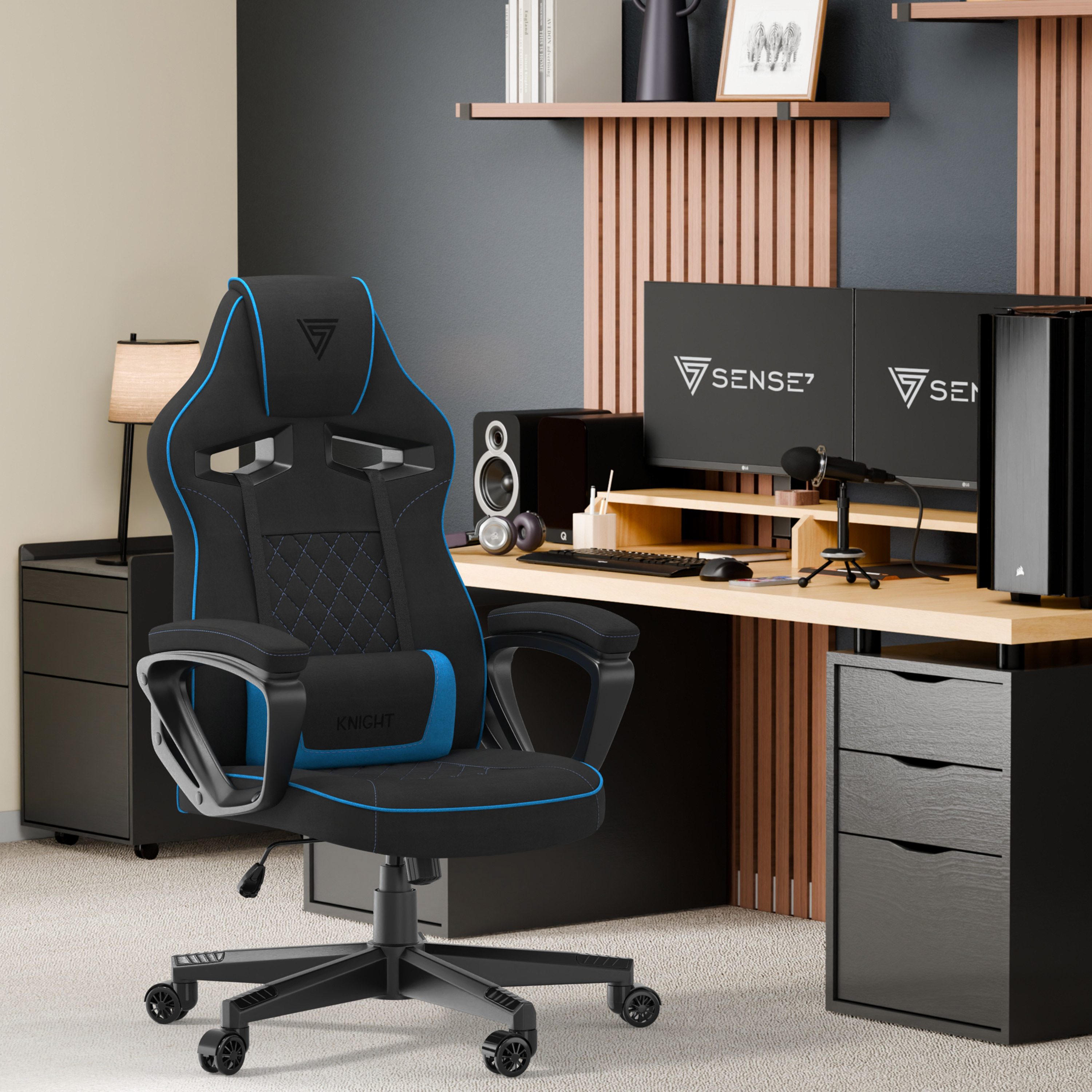 Chaise gaming dans un bureau à domicile. Chaise noire avec des touches de bleu, bureau avec moniteurs, enceintes et PC.