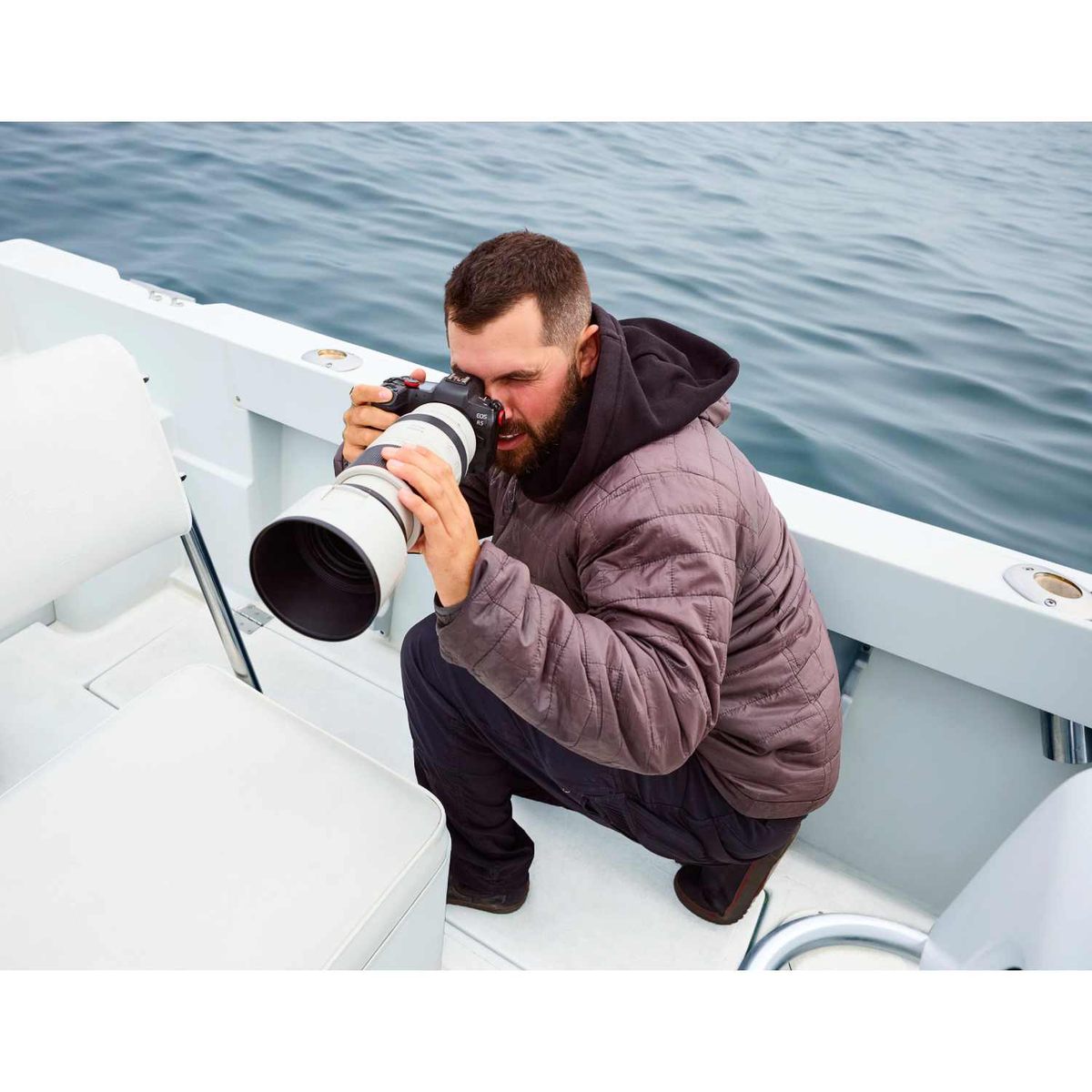 Ein Mann auf einem Boot fotografiert das Meer. Er trägt eine Jacke und benutzt eine Kamera mit langem Objektiv. Boot und Ozean sind sichtbar.