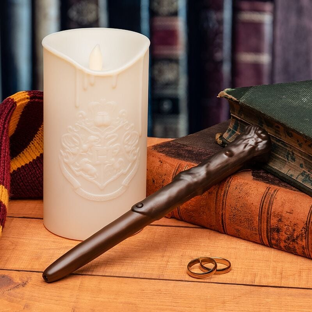 Kremowa świeca z herbem Hogwartu, różdżka, książki i pierścionki na drewnianej powierzchni.