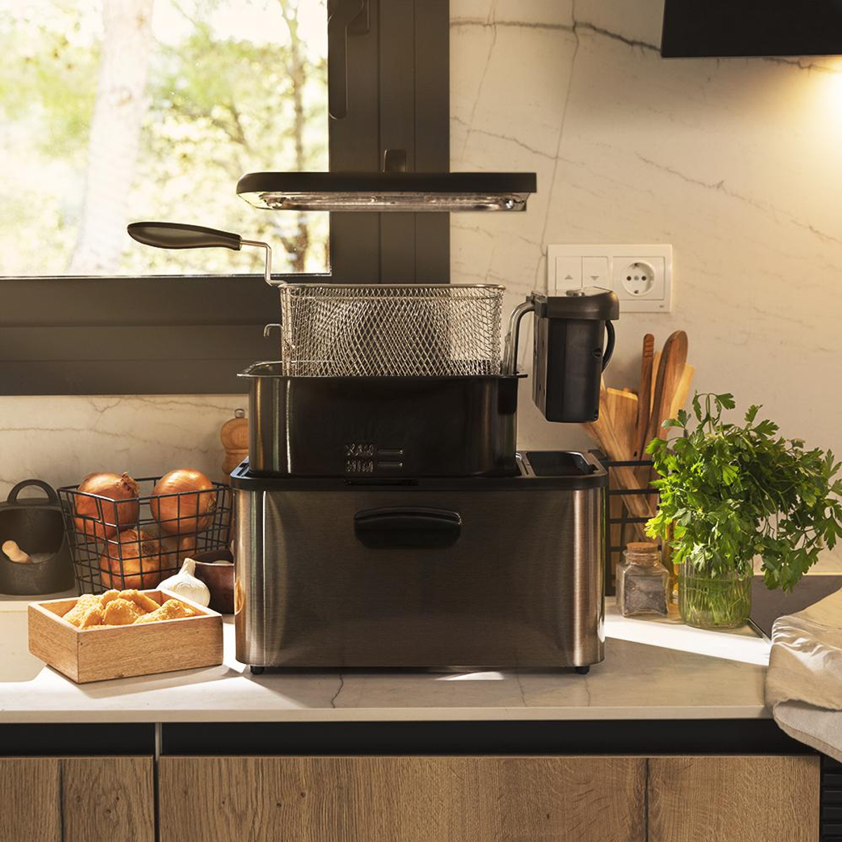 Scena kuchenna z frytownicą, cebulą i pietruszką. Frytownica stoi na blacie. W tle okno.