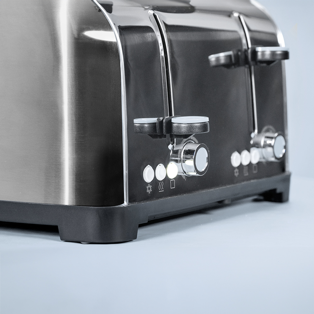 Zbliżenie na toster ze stali nierdzewnej z czarnymi akcentami. Ma wiele otworów, przycisków i pokręteł na jasnoniebieskim tle.