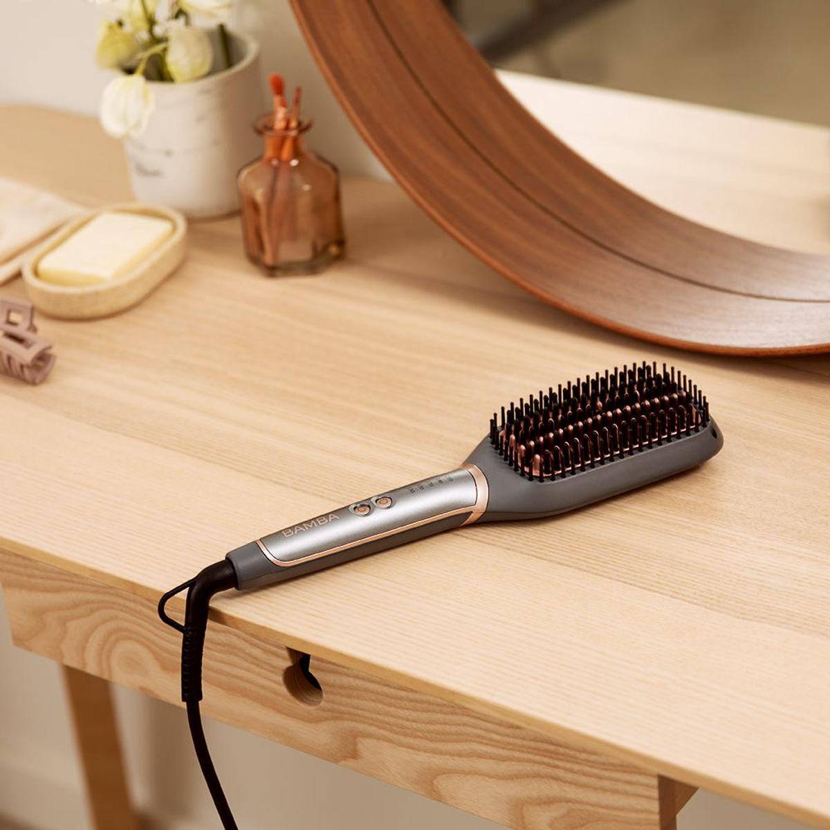 Una spazzola lisciante per capelli su un tavolo di legno. Uno specchio, fiori, sapone e un fermaglio per capelli sono visibili.