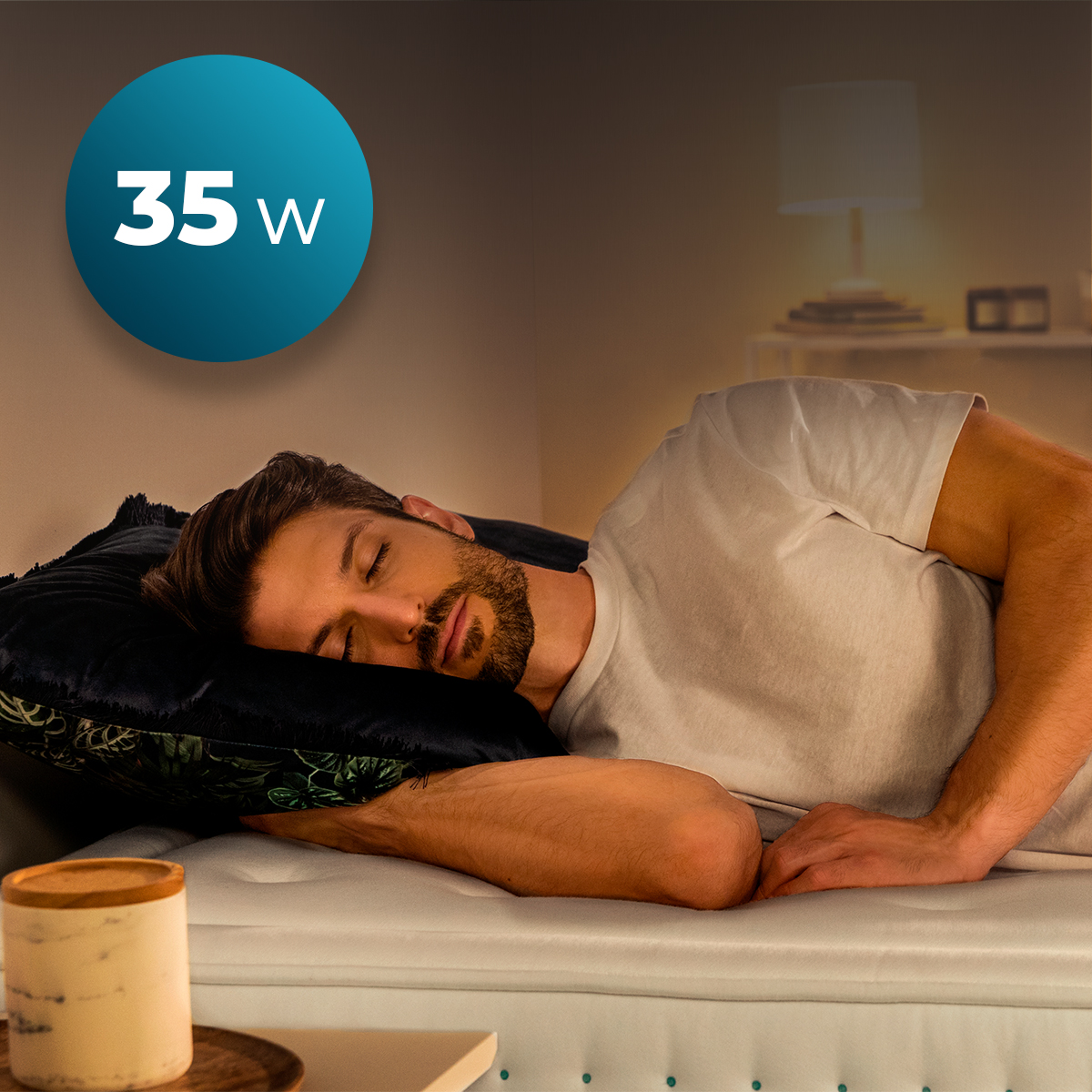 A man sleeps on a bed with a pillow. A blue circle with '35 w' is in the upper left. A lamp and side table are in the background.