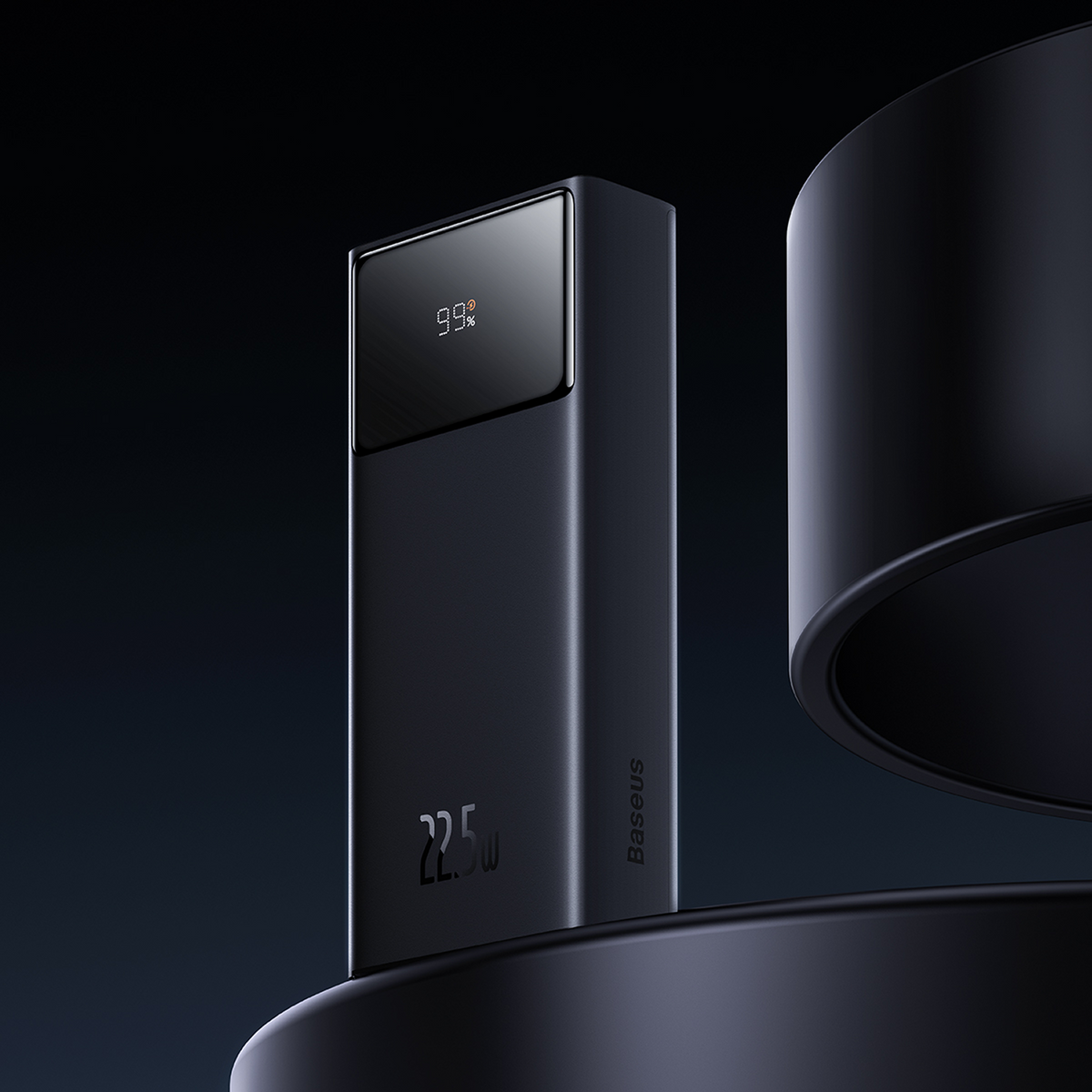 Un power bank nero Baseus mostra il 99% di carica. Ha un'uscita da 22,5W ed è posizionato su una superficie scura. Lo sfondo è scuro.