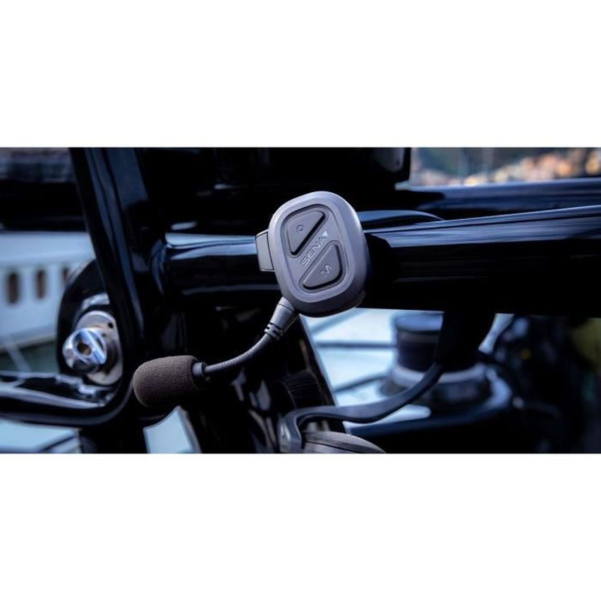 Primo piano di un sistema di comunicazione per moto Sena montato sul manubrio. Include un'unità di controllo e un microfono.