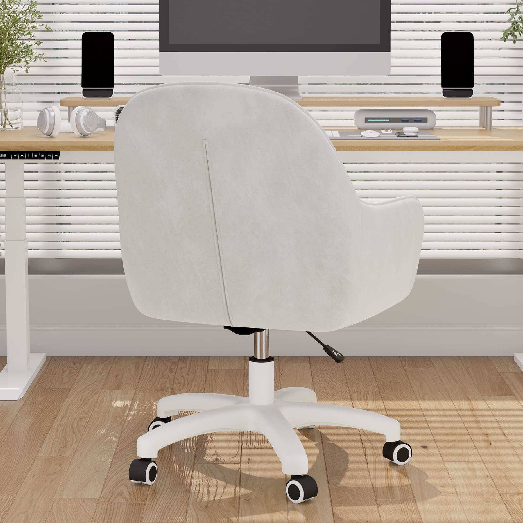 Silla de oficina blanca frente a una ventana con persianas. Escritorio con monitor, altavoces y auriculares. Suelo de madera.