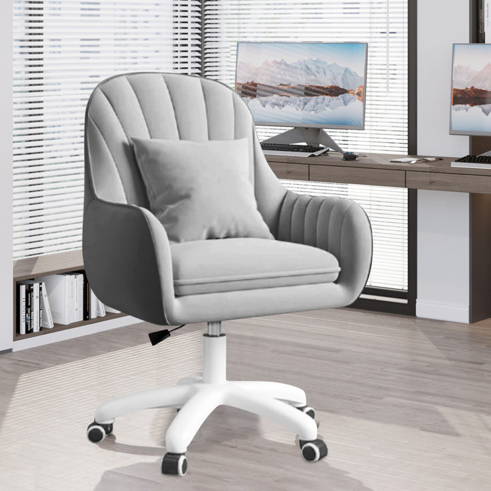 Una silla de oficina gris con base y ruedas blancas. Una almohada está en la silla. Dos monitores y un escritorio en el fondo.
