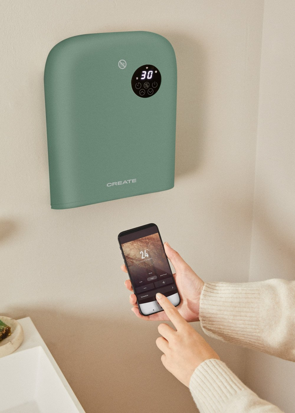 Un calentador verde montado en la pared muestra 30 grados. Una mano usa un teléfono para controlar el calentador, mostrando 24 grados.