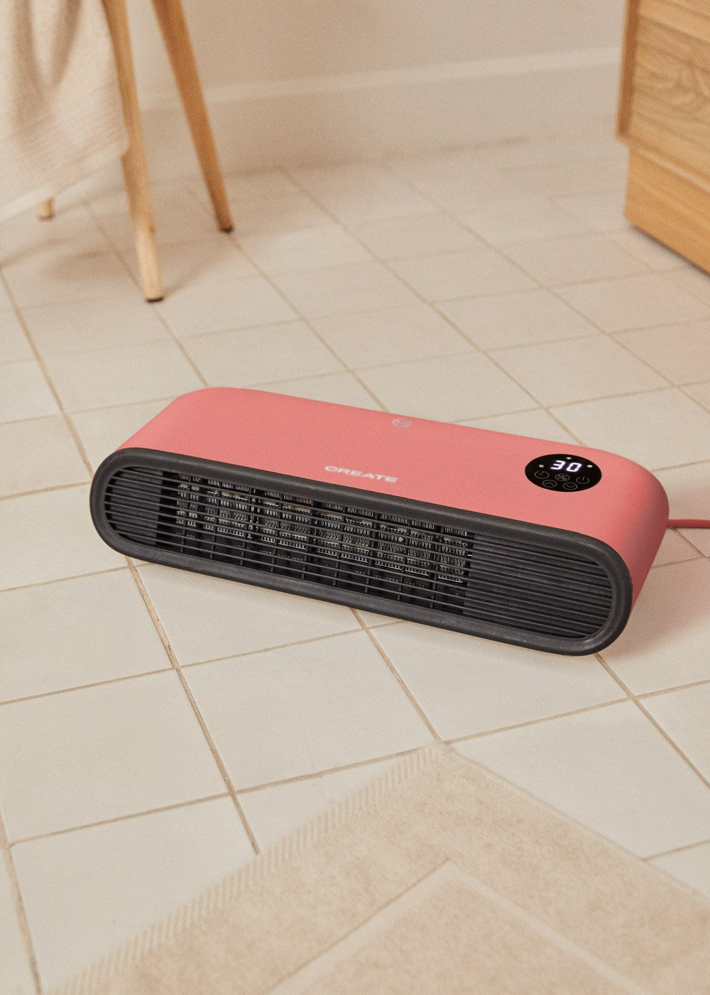 Un calefactor eléctrico rosa sobre baldosas blancas. Tiene una rejilla negra y una pantalla digital que muestra 30 grados.