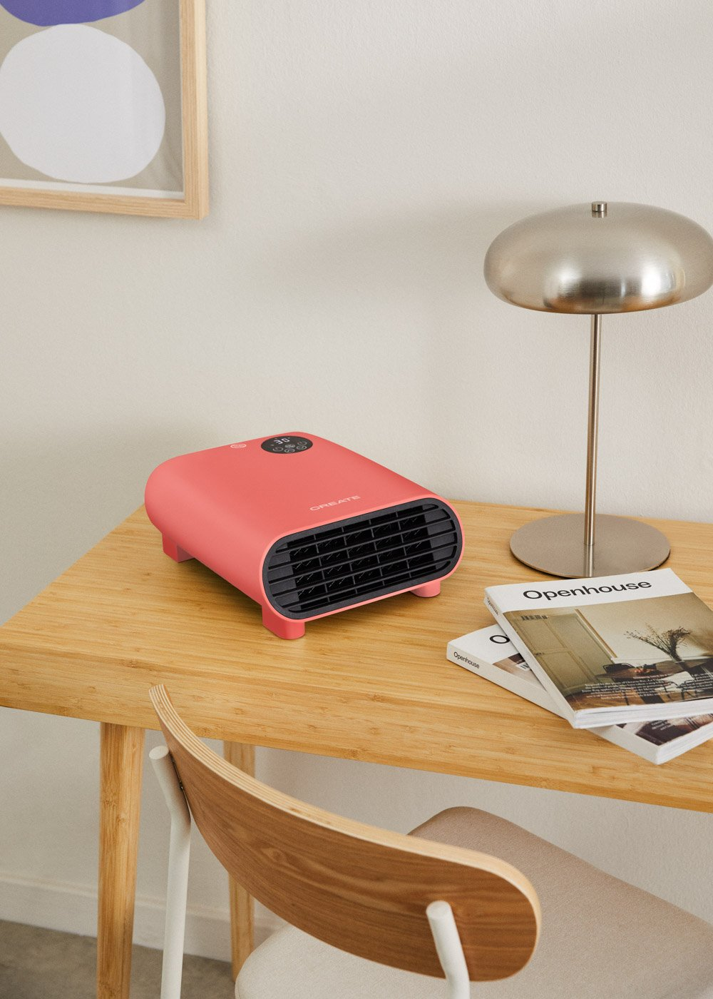 Un calefactor rosa sobre un escritorio de madera con lámpara, libros y silla. Un cuadro cuelga en la pared.