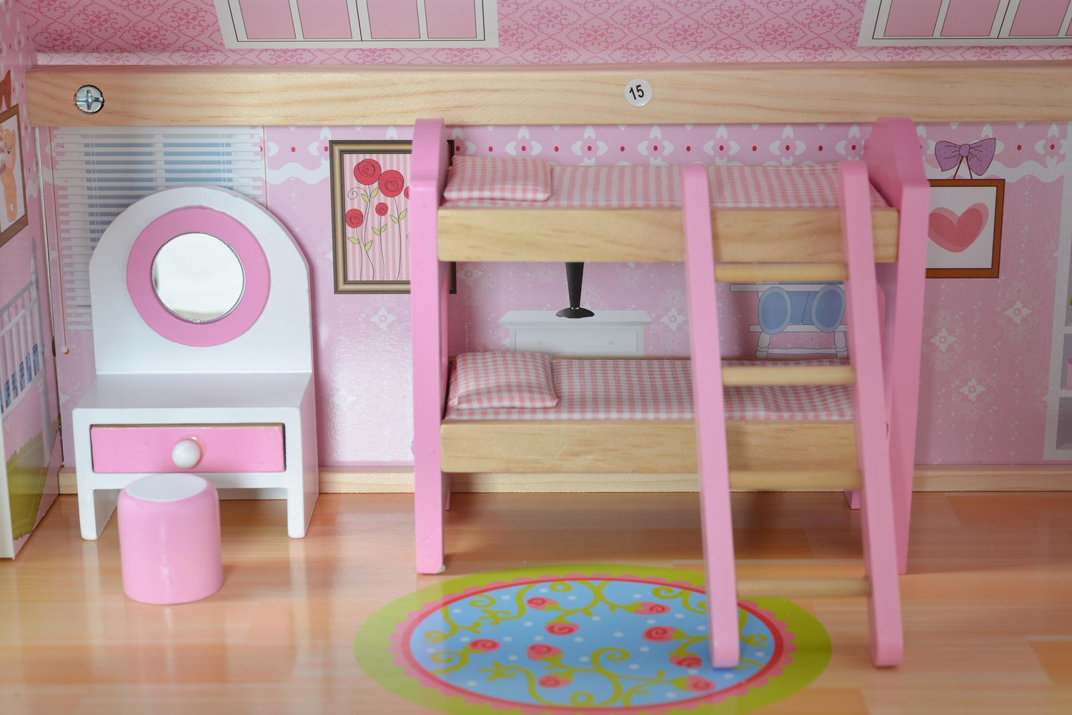 Ein Puppenhaus-Innenraum mit rosa Etagenbetten, einem Schminktisch und einem runden Teppich auf Holzboden.