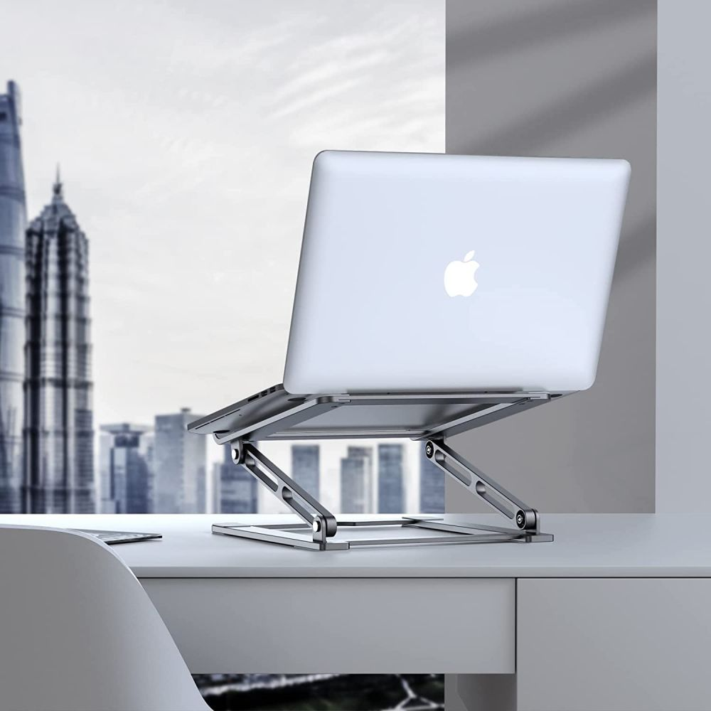 A silver laptop on a silver stand, with a city skyline in the background. The laptop displays the Apple logo.