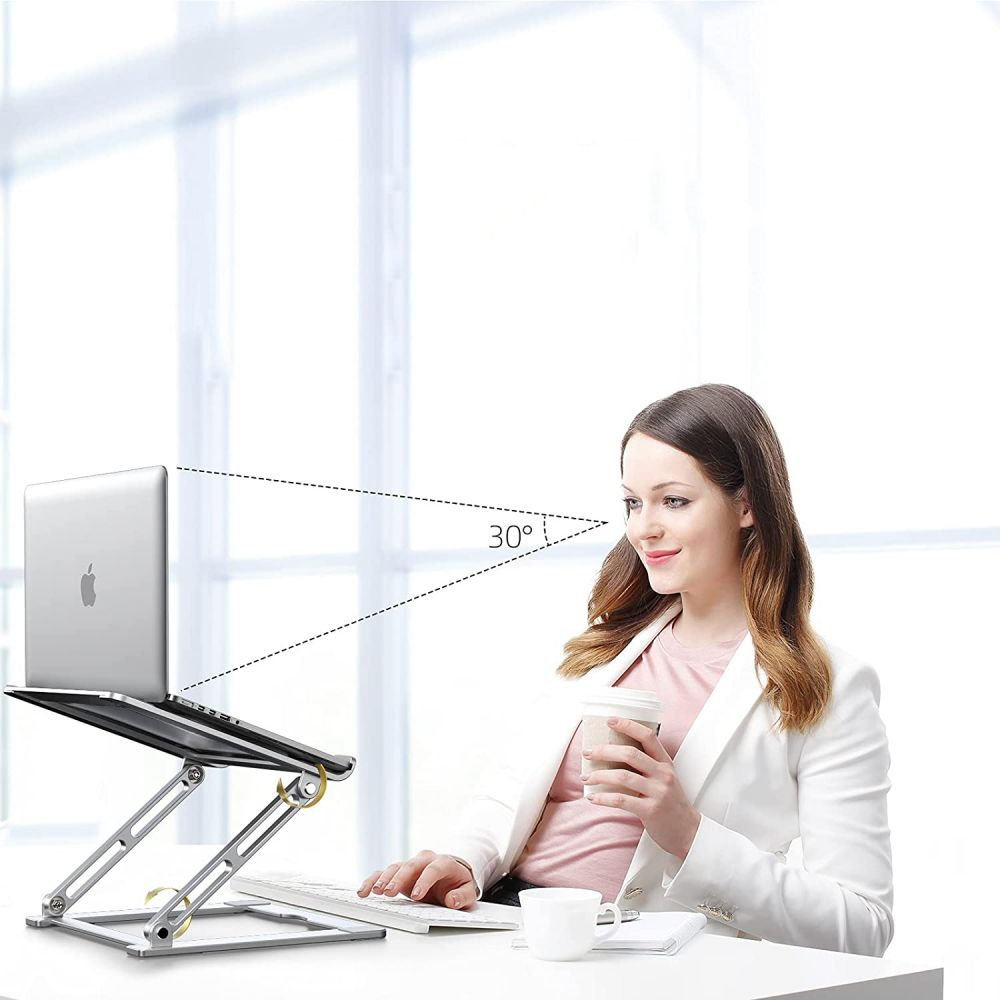Woman uses laptop on a stand, holding coffee. A white desk with keyboard and cup. Angle of view is 30 degrees.