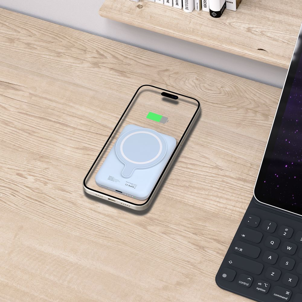 Un téléphone avec un chargeur bleu clair est sur un bureau en bois. Une tablette et des livres sont également visibles en arrière-plan.