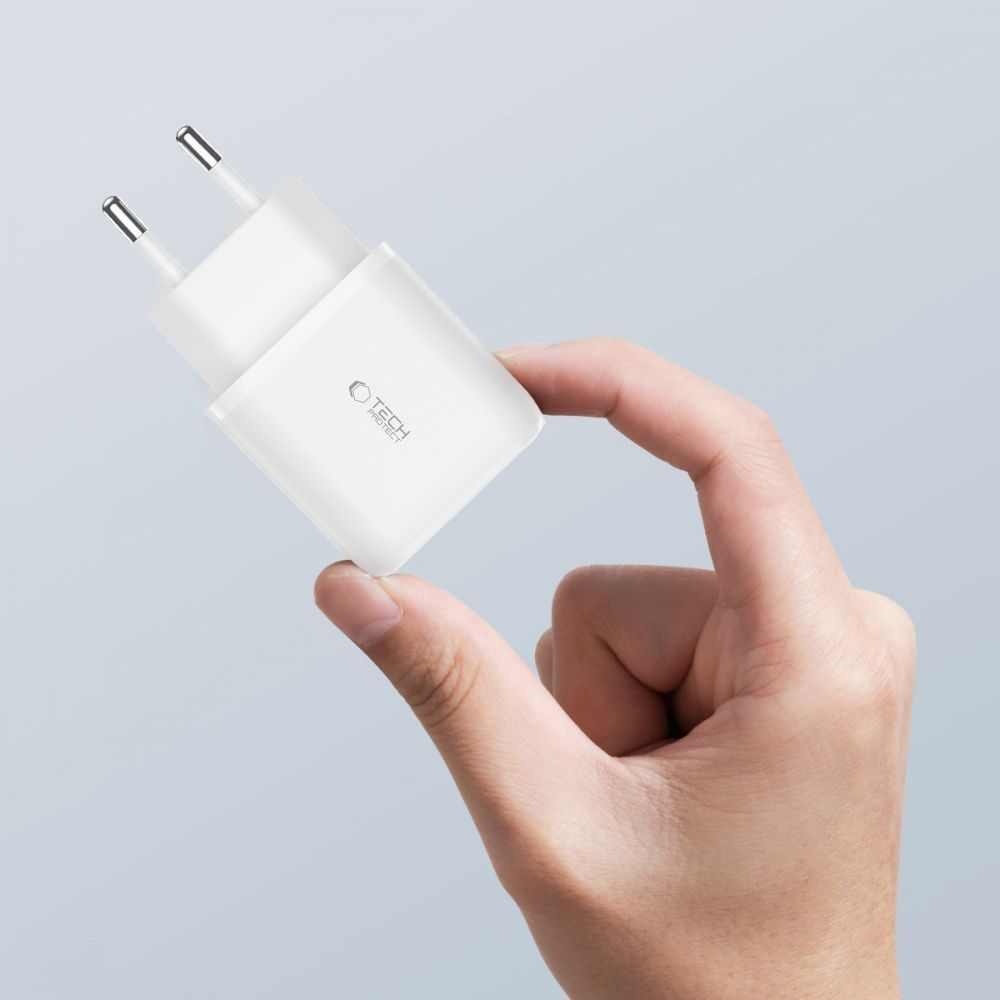 Une main tient un chargeur de téléphone blanc avec deux broches. Le chargeur porte l'inscription 'TECH PROTECT'.