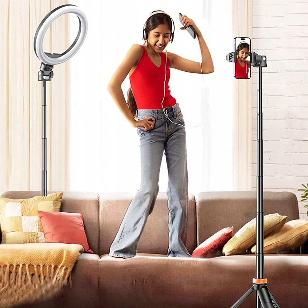 Een meisje in een rode top en jeans neemt een video op. Ze staat in de buurt van een ringlicht en een telefoon op een statief.